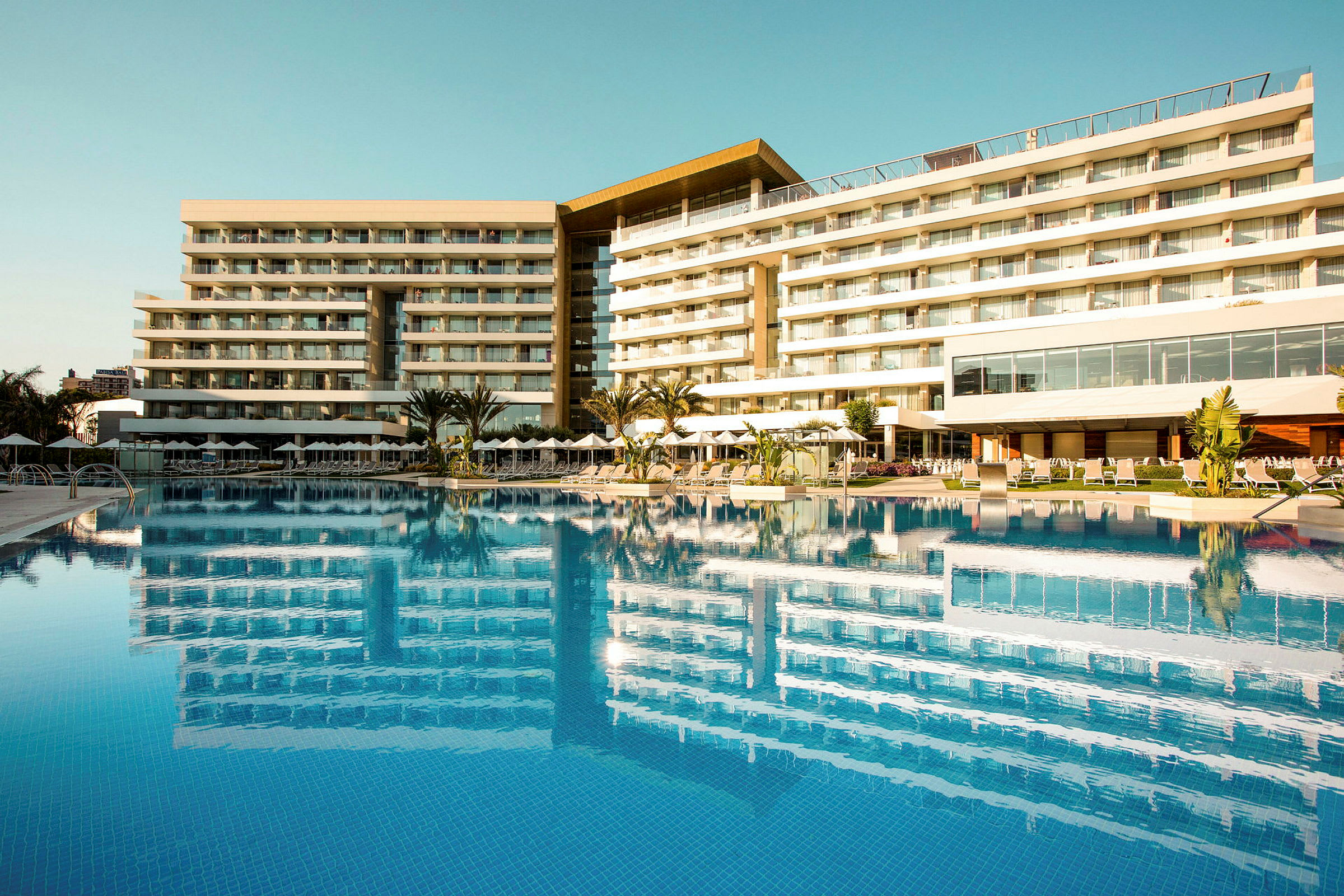 Et moderne hotel med altaner ved en stor pool. (AI-genereret tekst)