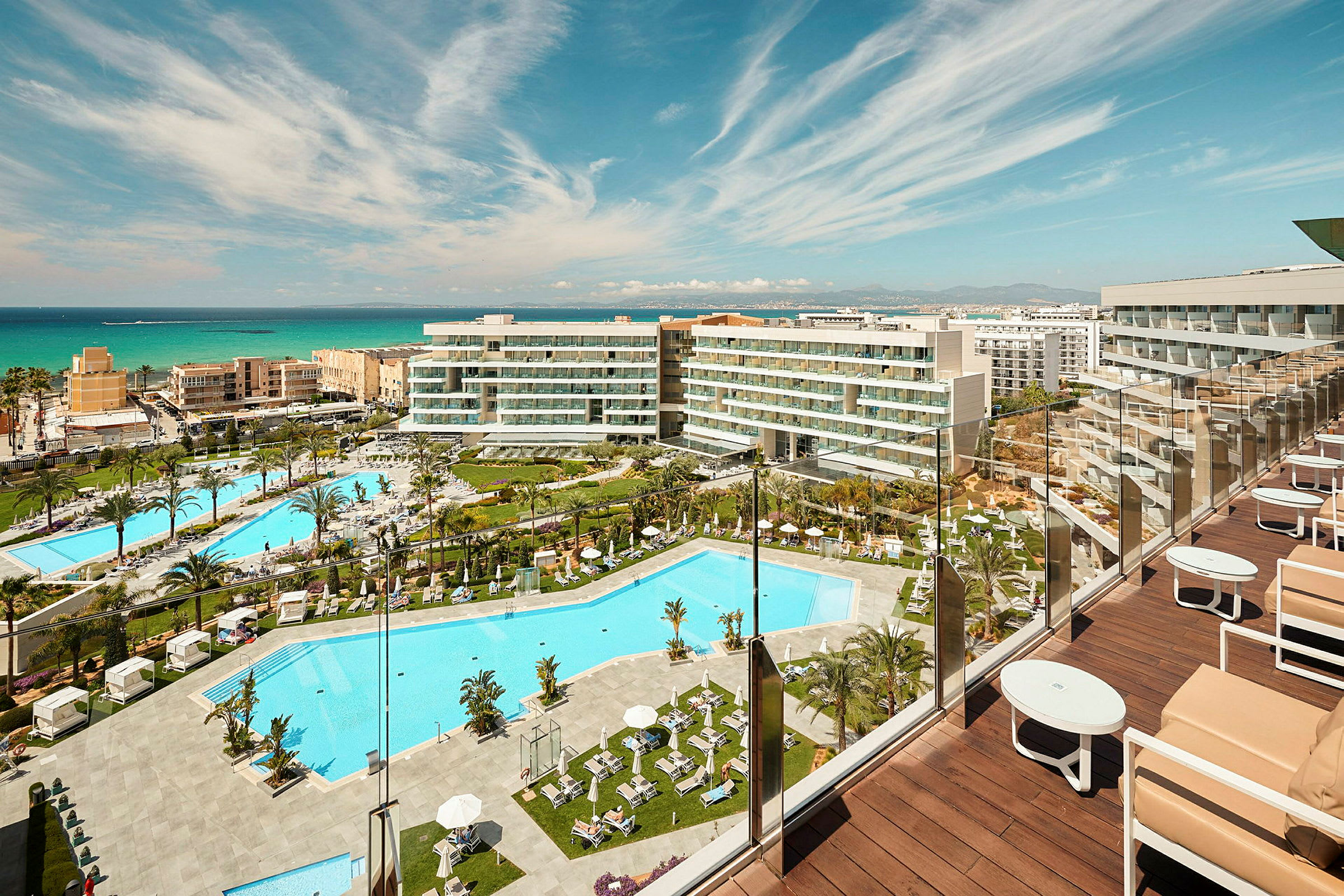 Udsigt over hotelområde med flere pools og bygninger tæt på havet. (AI-genereret tekst)