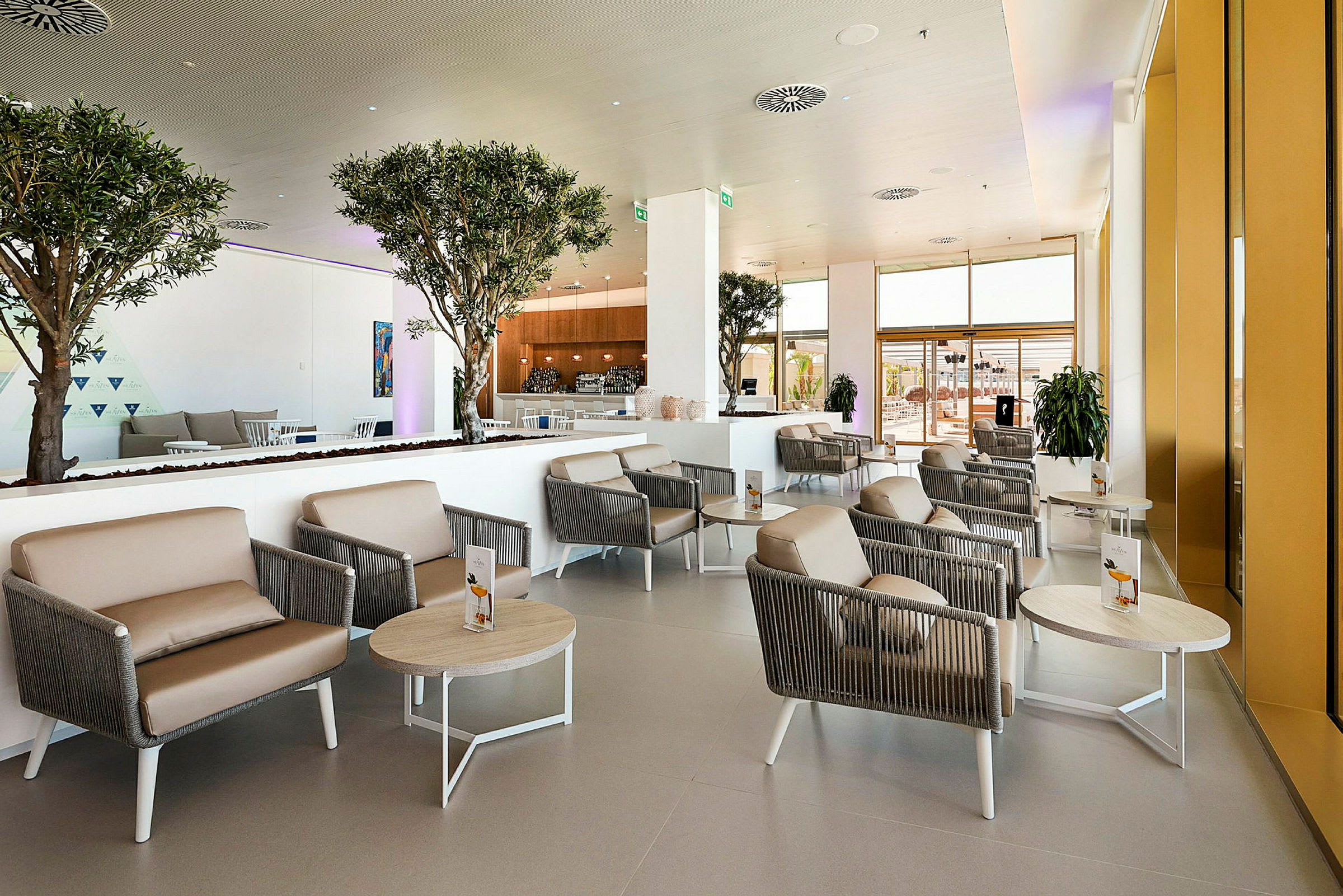 Moderne og lyst hotellobbyområde med siddegrupper og indendørs træer. (AI-genereret tekst)