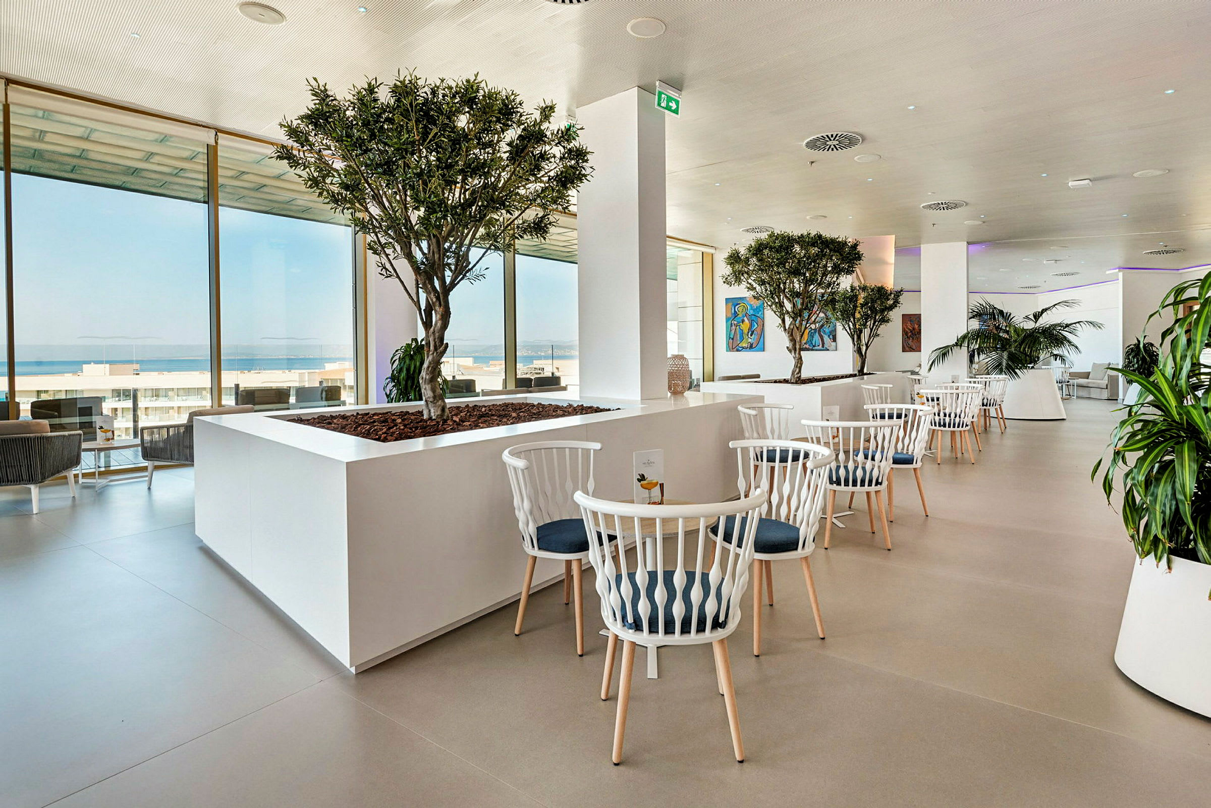 Elegant restaurant med hvide møbler, grønne planter og store vinduer med udsigt. (AI-genereret tekst)