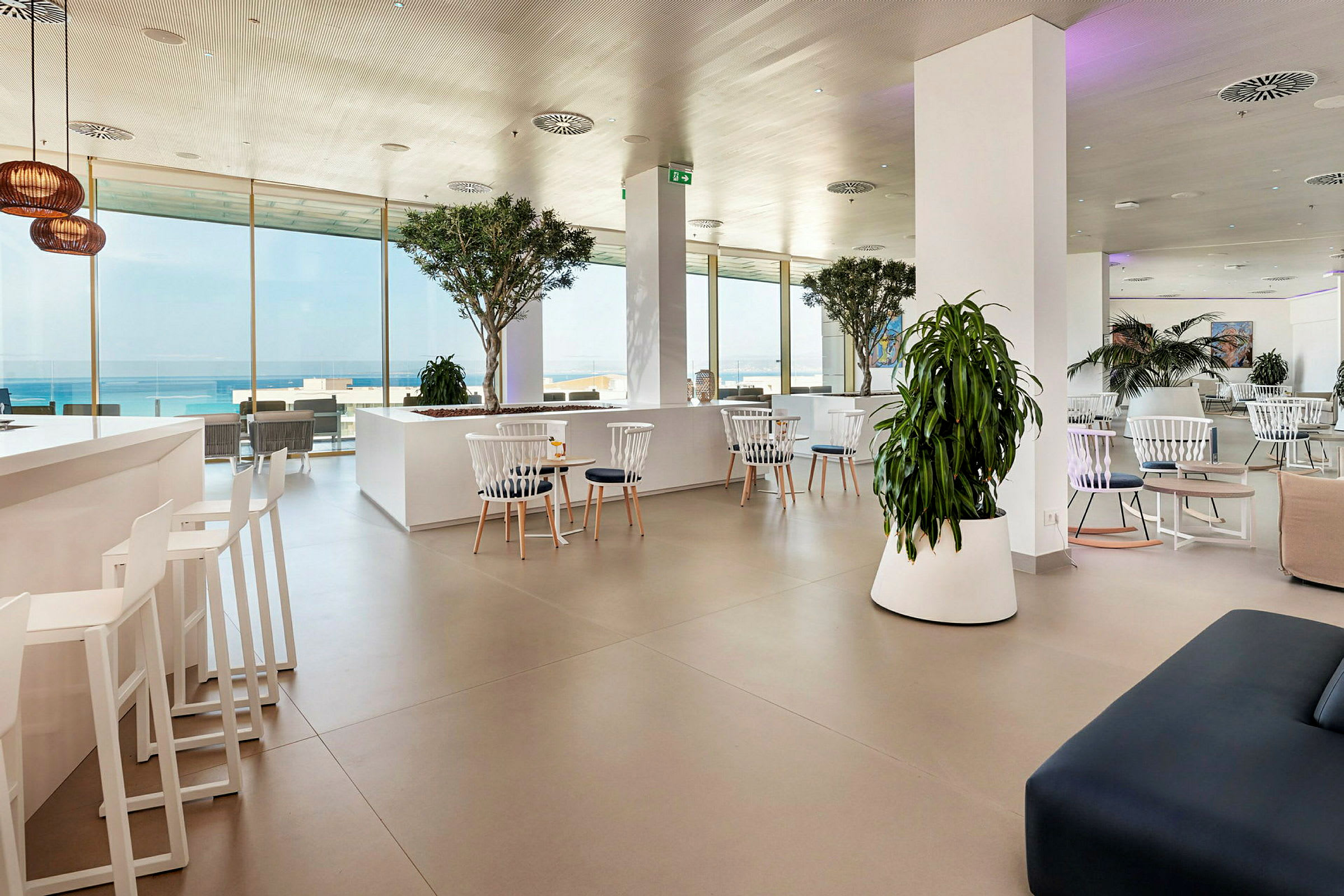 Moderne lounge med hvide møbler og grønne planter, havudsigt gennem store vinduer. (AI-genereret tekst)