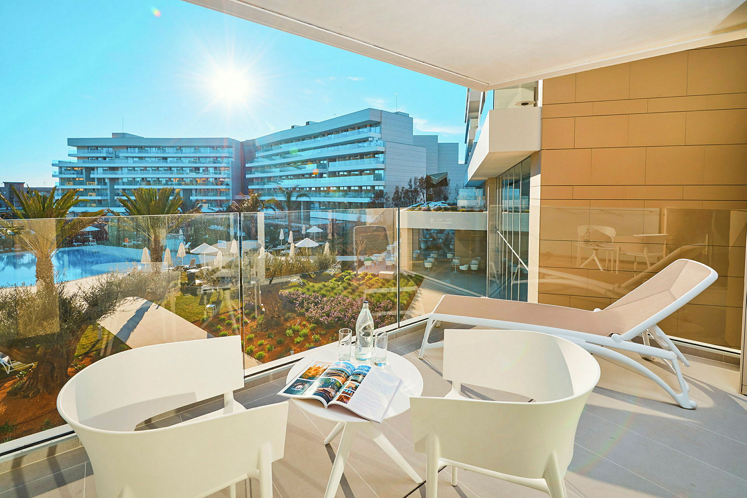 Udsigt fra en altan med bord og stole over et hotelområde med swimmingpool. (AI-genereret tekst)