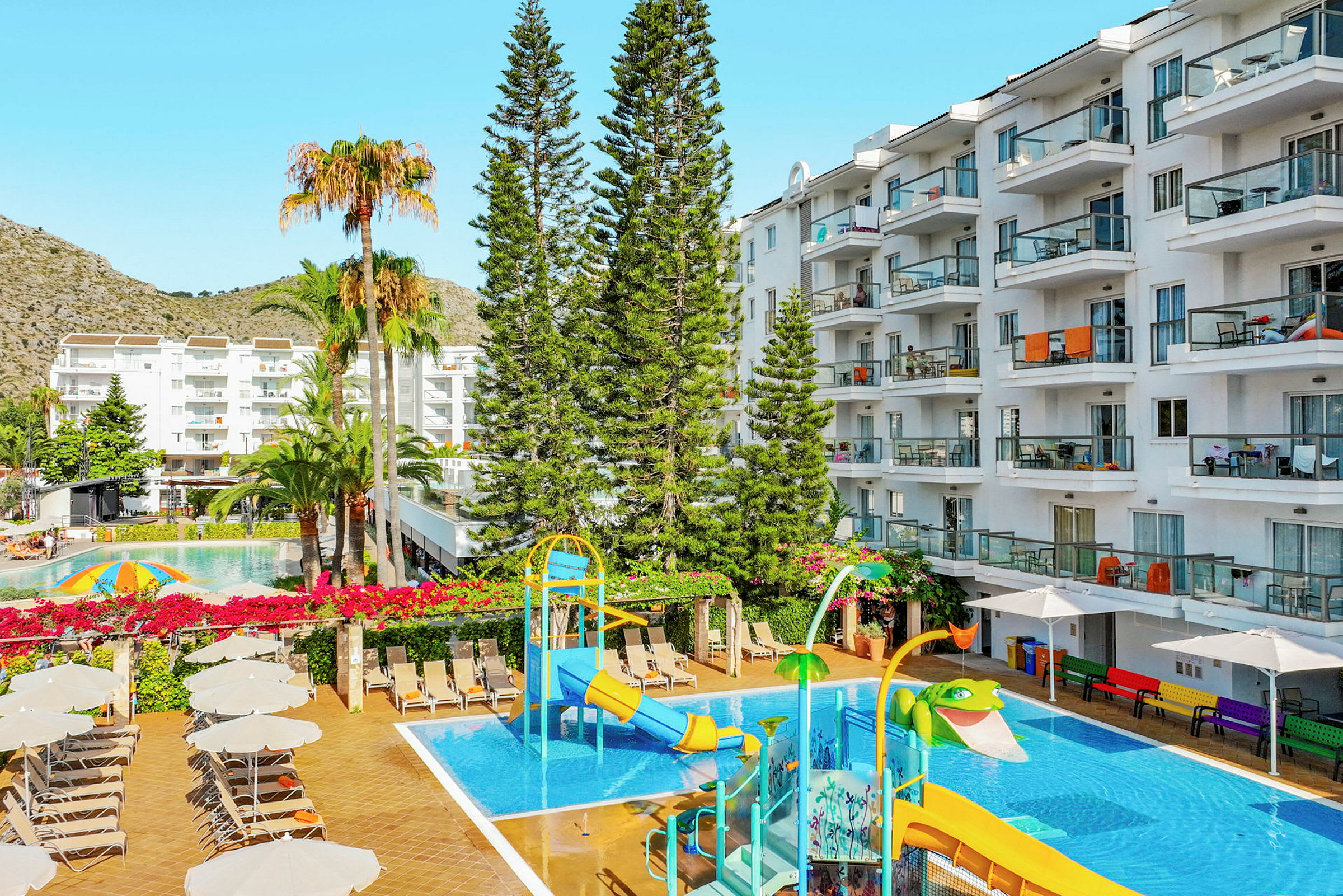 Udsigt over hotellets poolområde med vandrutsjebane, liggestole og omkringliggende bygninger. (AI-genereret tekst)