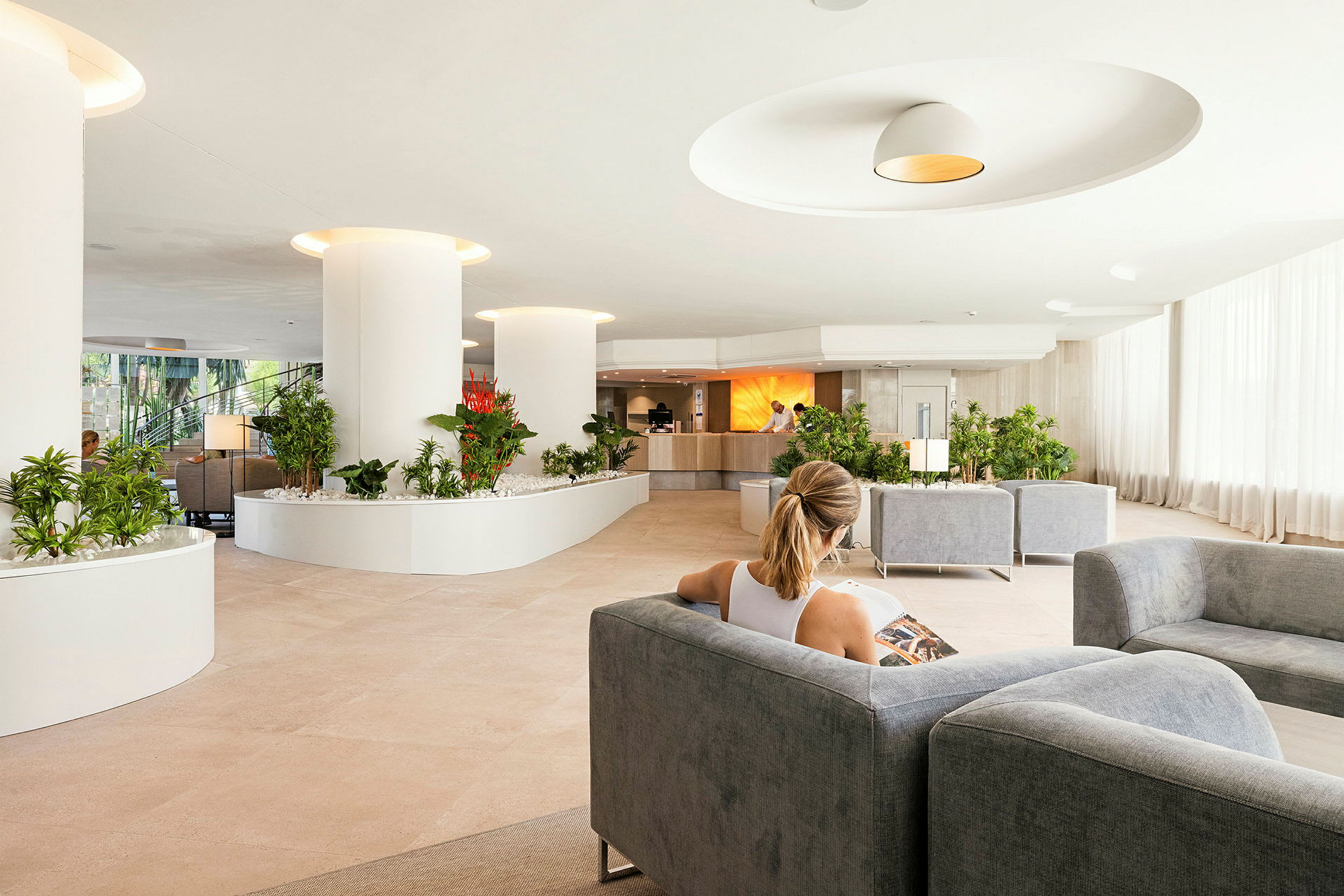 Person sidder i en rummelig hotellobby med moderne indretning og grønne planter. (AI-genereret tekst)