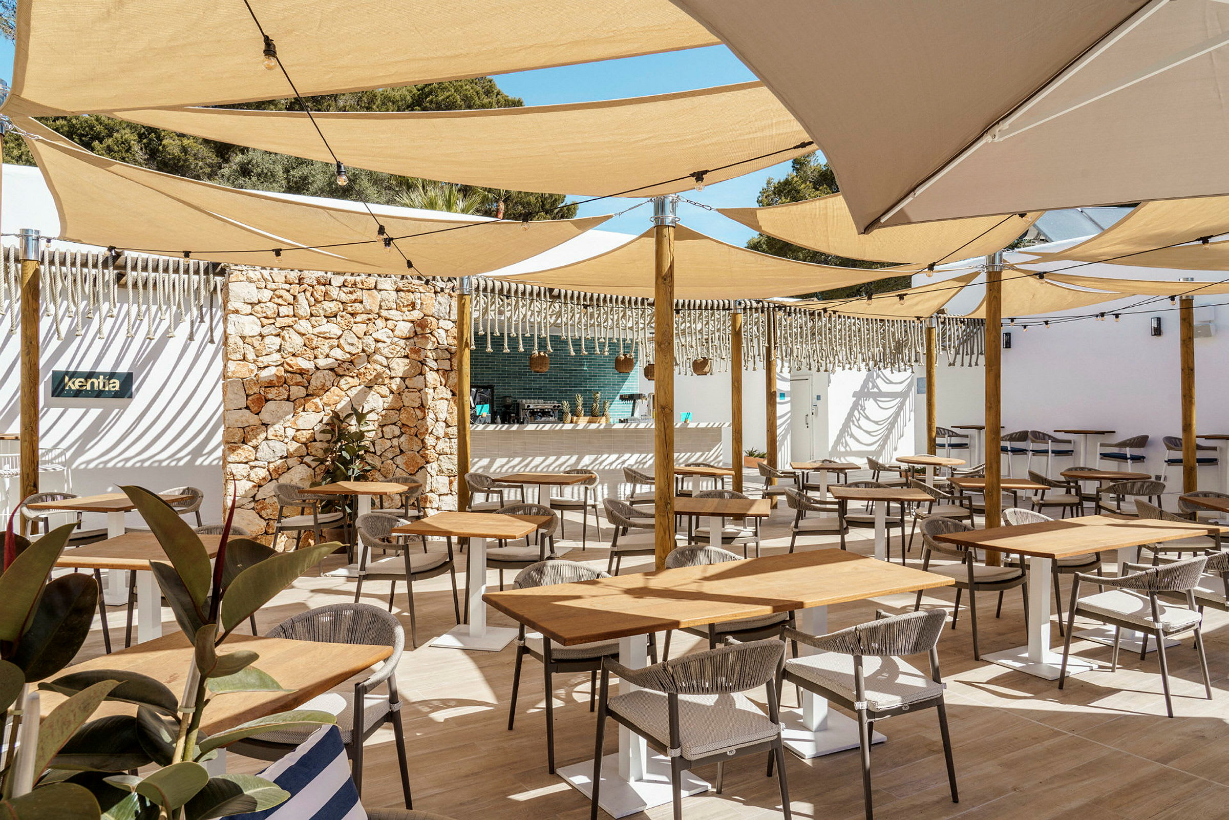 En udendørs restaurant med borde og stole under skyggefulde sejlduge. (AI-genereret tekst)