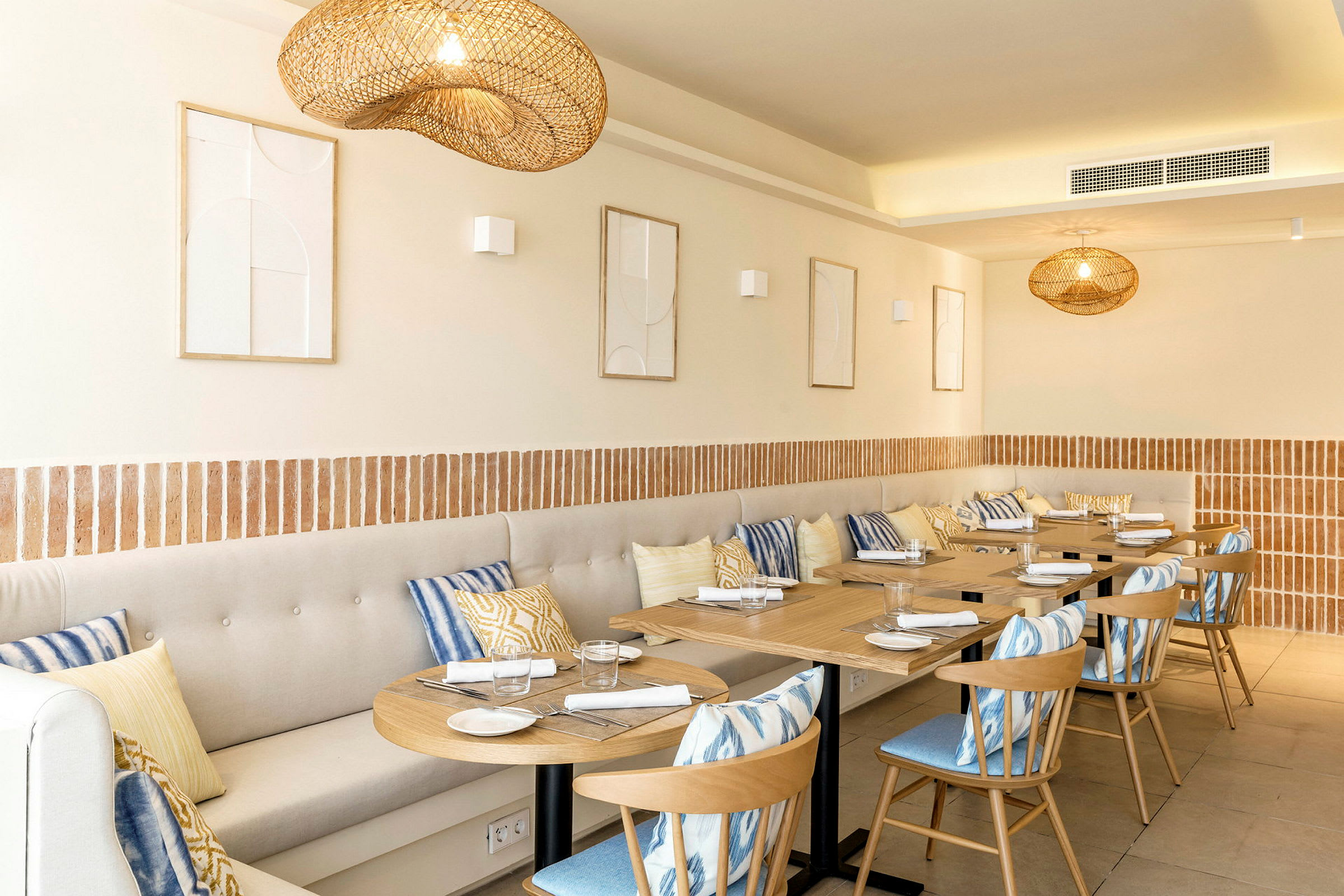 En restaurant med træborde, stole og beige siddebænke dekoreret med farverige puder. (AI-genereret tekst)