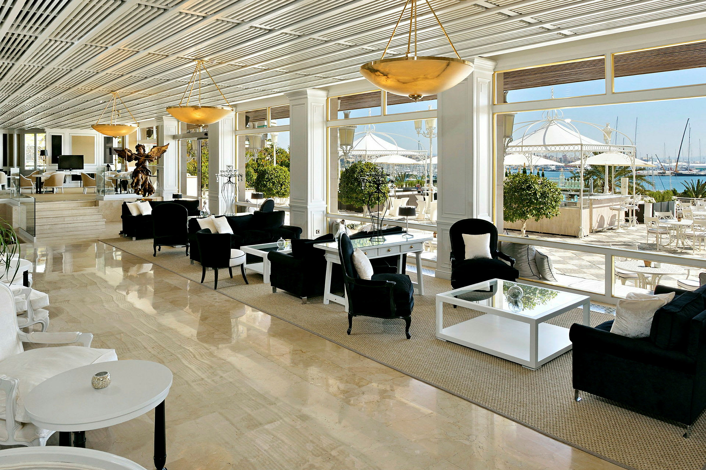 En elegant indrettet lounge med store vinduer, der giver udsigt til en terrasse og en marina. (AI-genereret tekst)