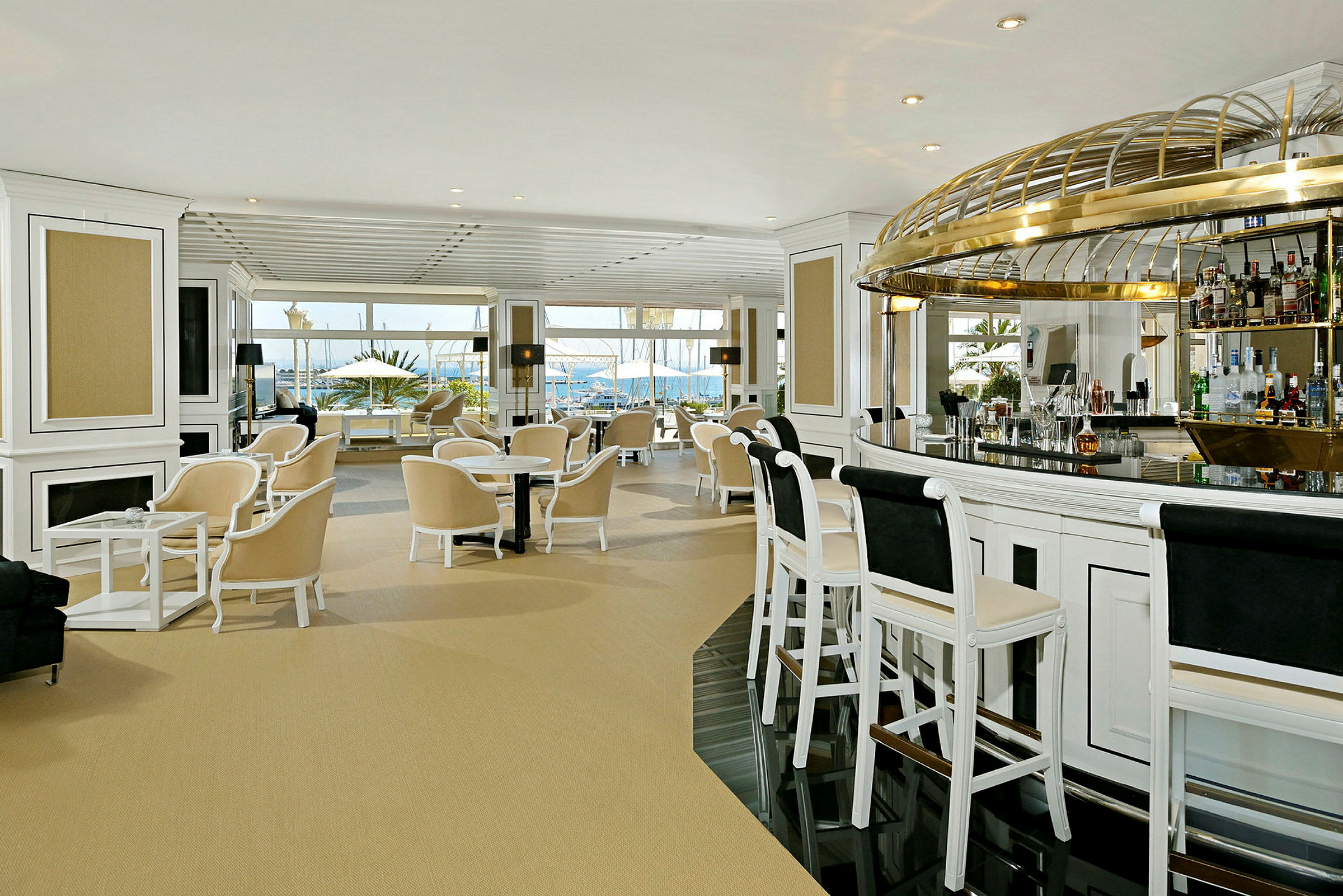 Interiør af en elegant hotelbar med lyse møbler og store vinduer ud mod havet. (AI-genereret tekst)