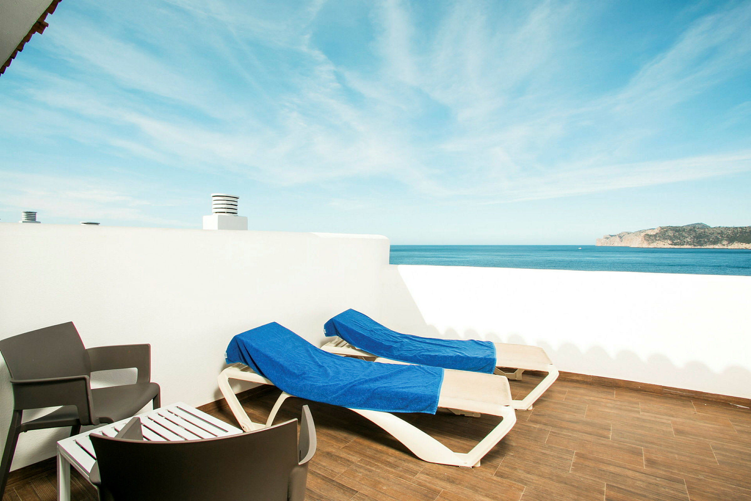 To liggestole med blå håndklæder på en terrasse med udsigt over havet. (AI-genereret tekst)