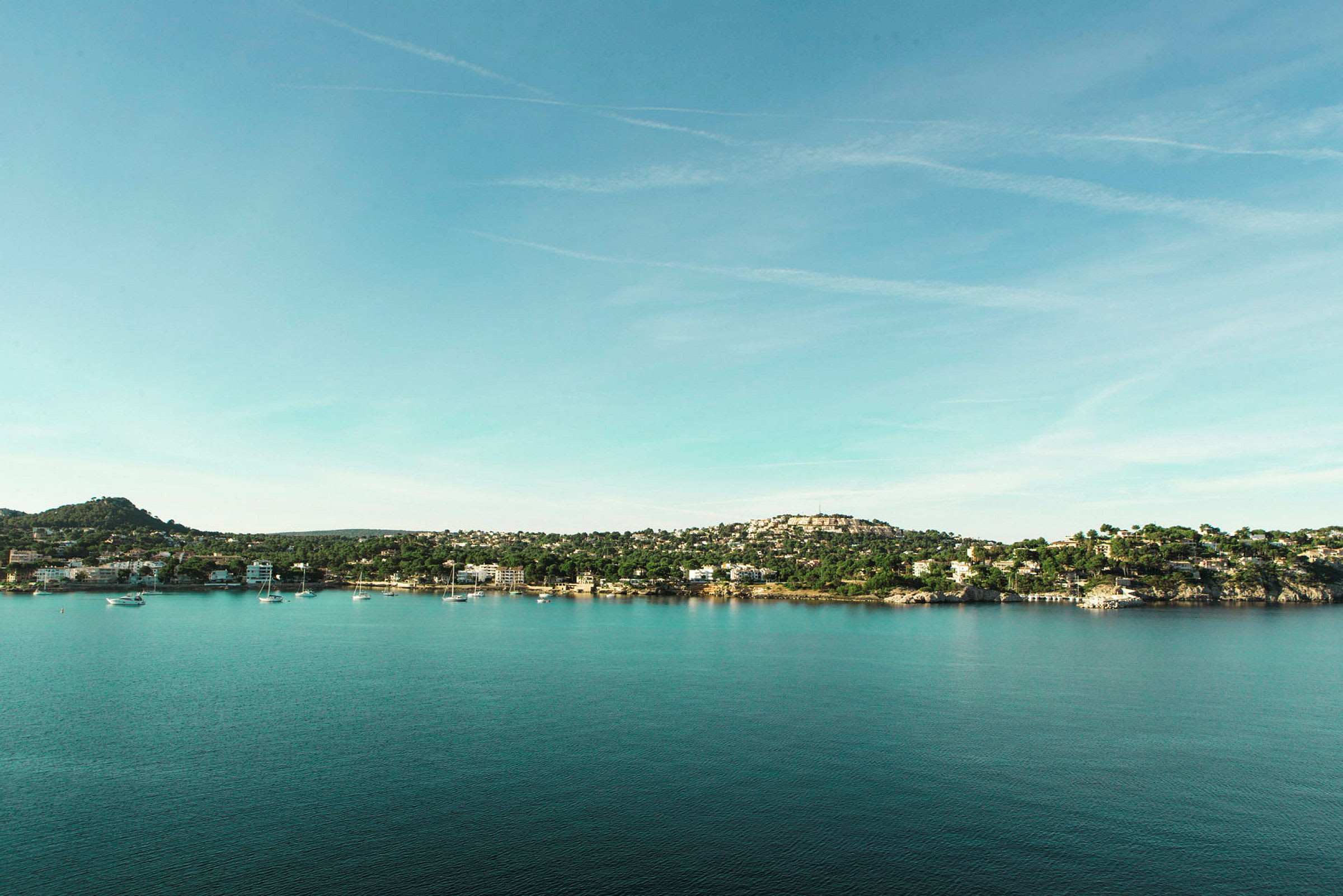 Udsigt over en kystlinje med huse og både ved vandet under en klar himmel. (AI-genereret tekst)