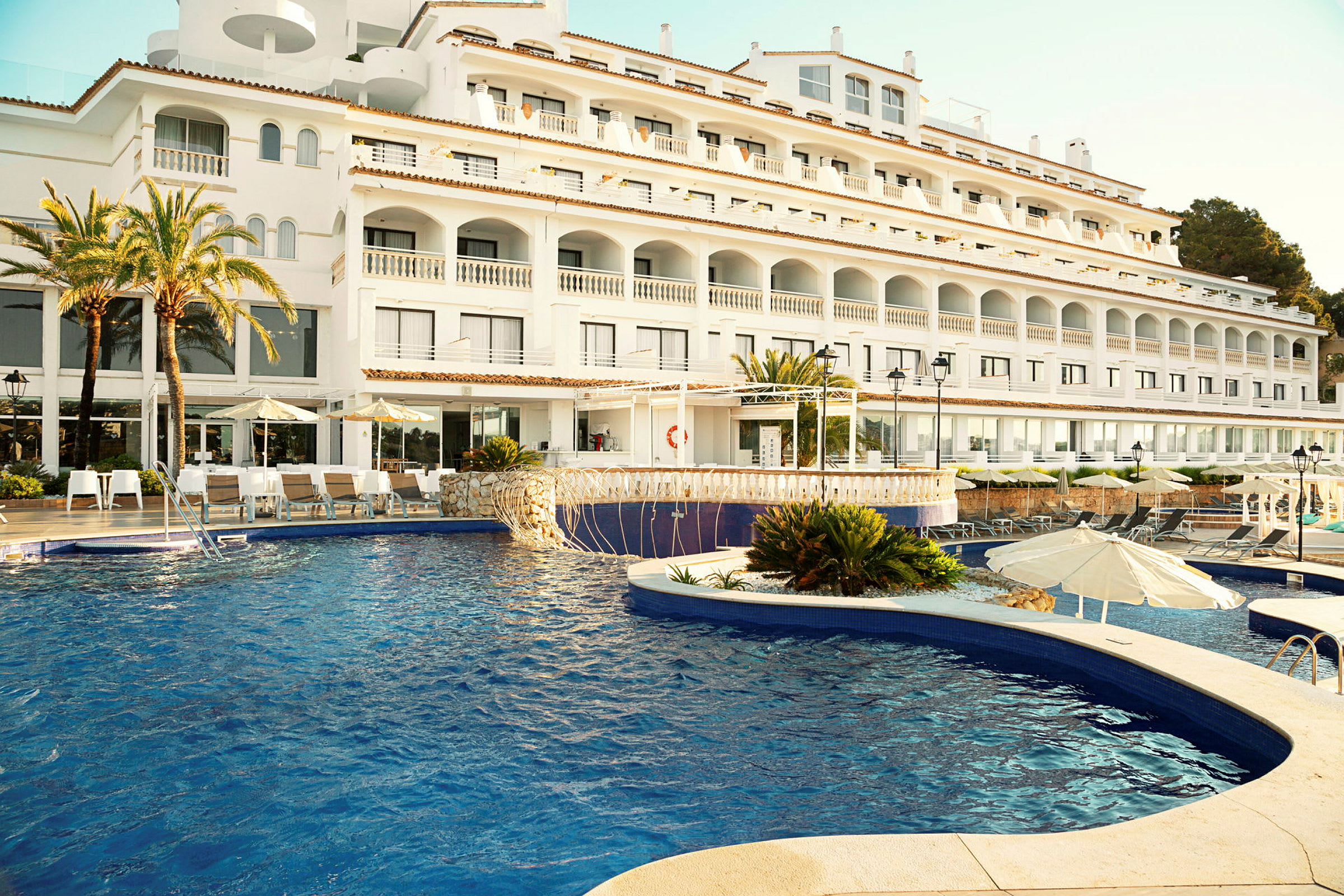 Hotel med hvid facade og swimmingpool i forgrunden. (AI-genereret tekst)