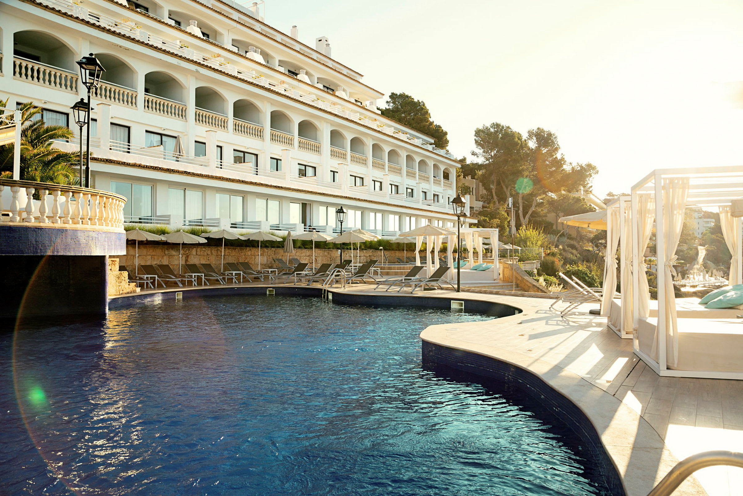 En moderne hotelbygning med en udendørs pool og liggestole under parasoller. (AI-genereret tekst)