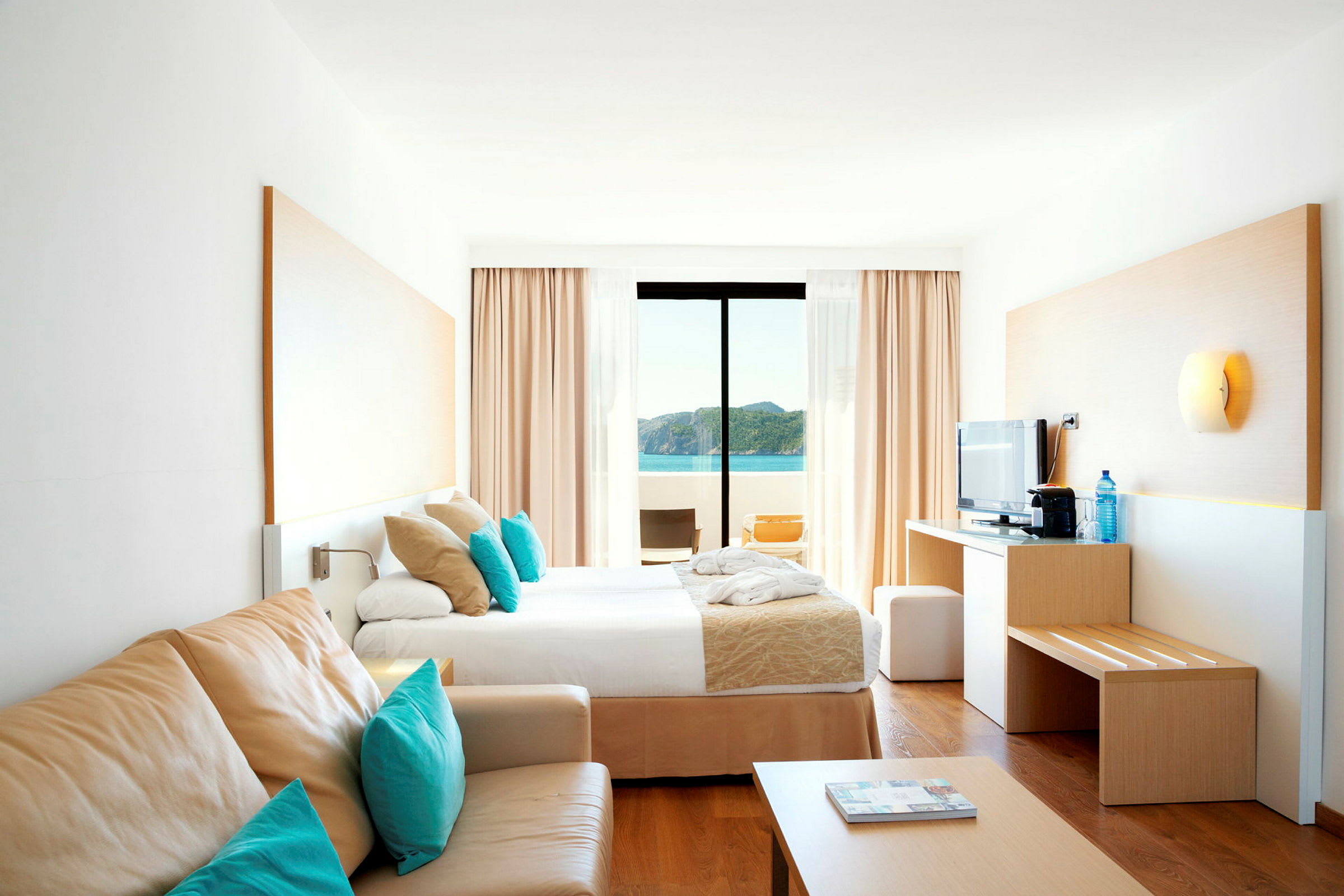 Et lyst hotelværelse med en seng, sofa og udsigt over havet. (AI-genereret tekst)