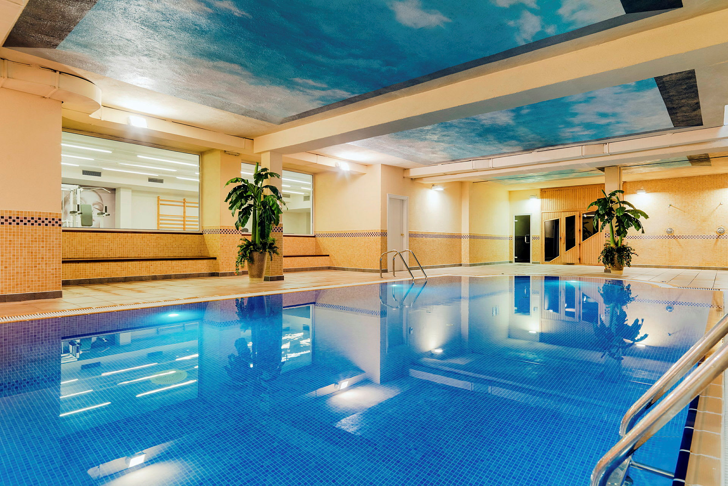 Indendørs pool med mosaikfliser, omgivet af beige vægge og dekorative planter. (AI-genereret tekst)
