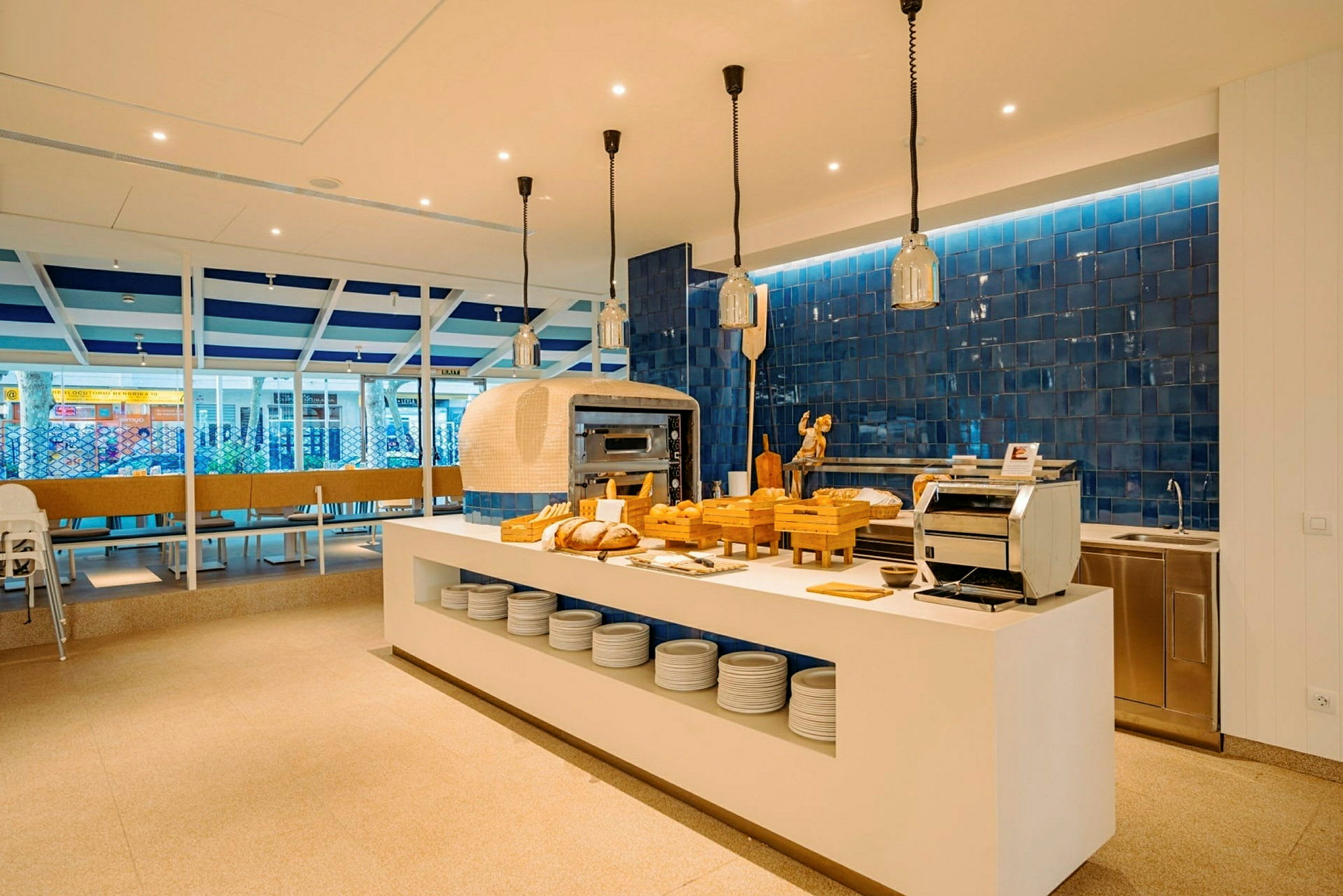 Moderne restaurantmiljø med et åbent køkken og spiseborde i fokus. Brød og køkkenudstyr er placeret på en hvid bænk. (AI-genereret tekst)