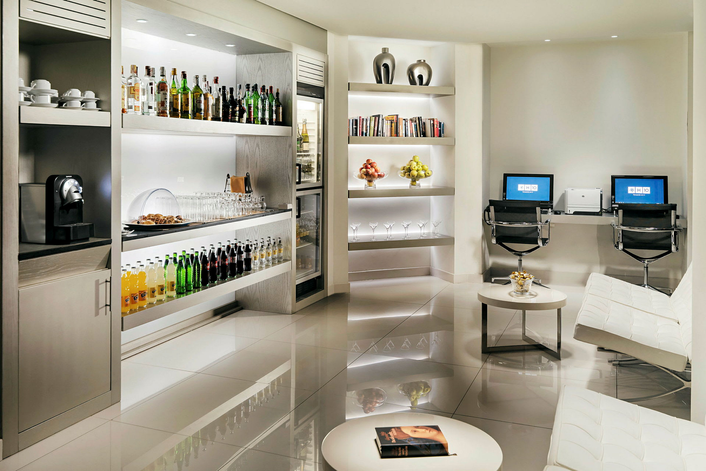 Et elegant indrettet rum med veludstyrede hylder med drikkevarer og frugt, en siddegruppe og to computerarbejdsstationer. (AI-genereret tekst)