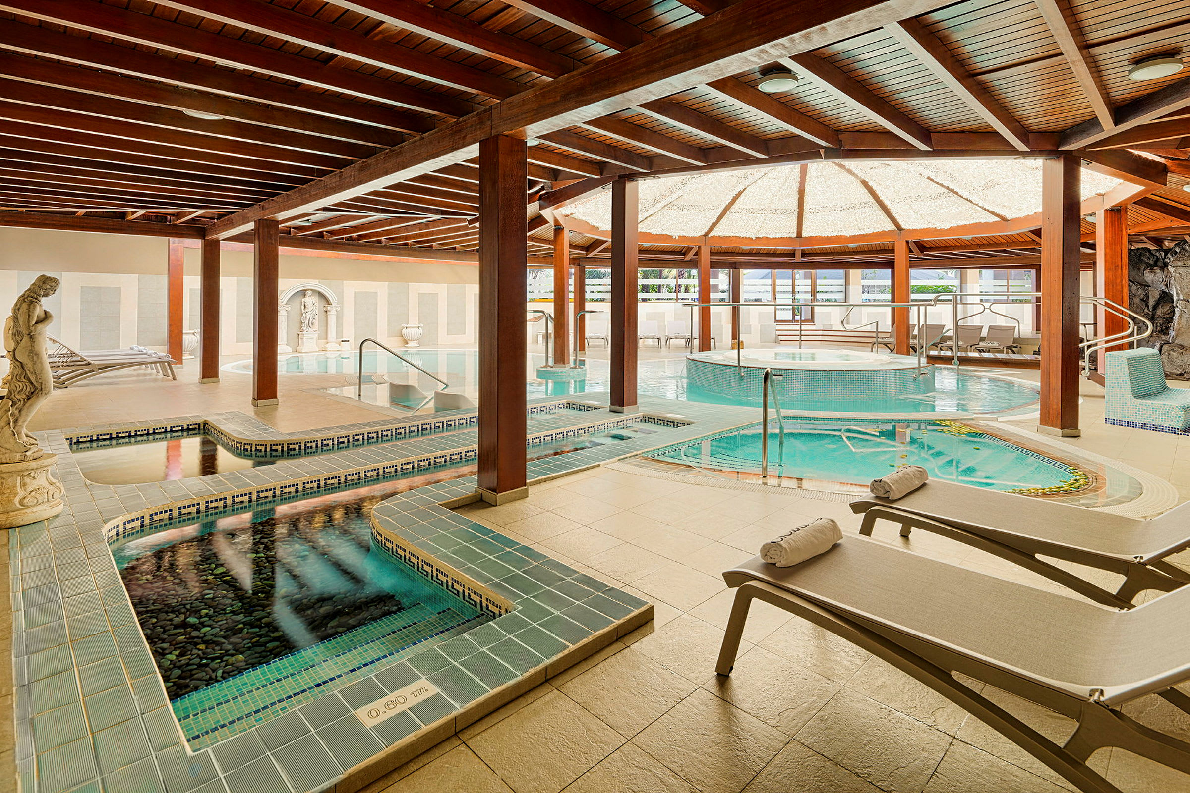 Interiør af et spa med flere pools, liggestole og elegant indretning. (AI-genereret tekst)