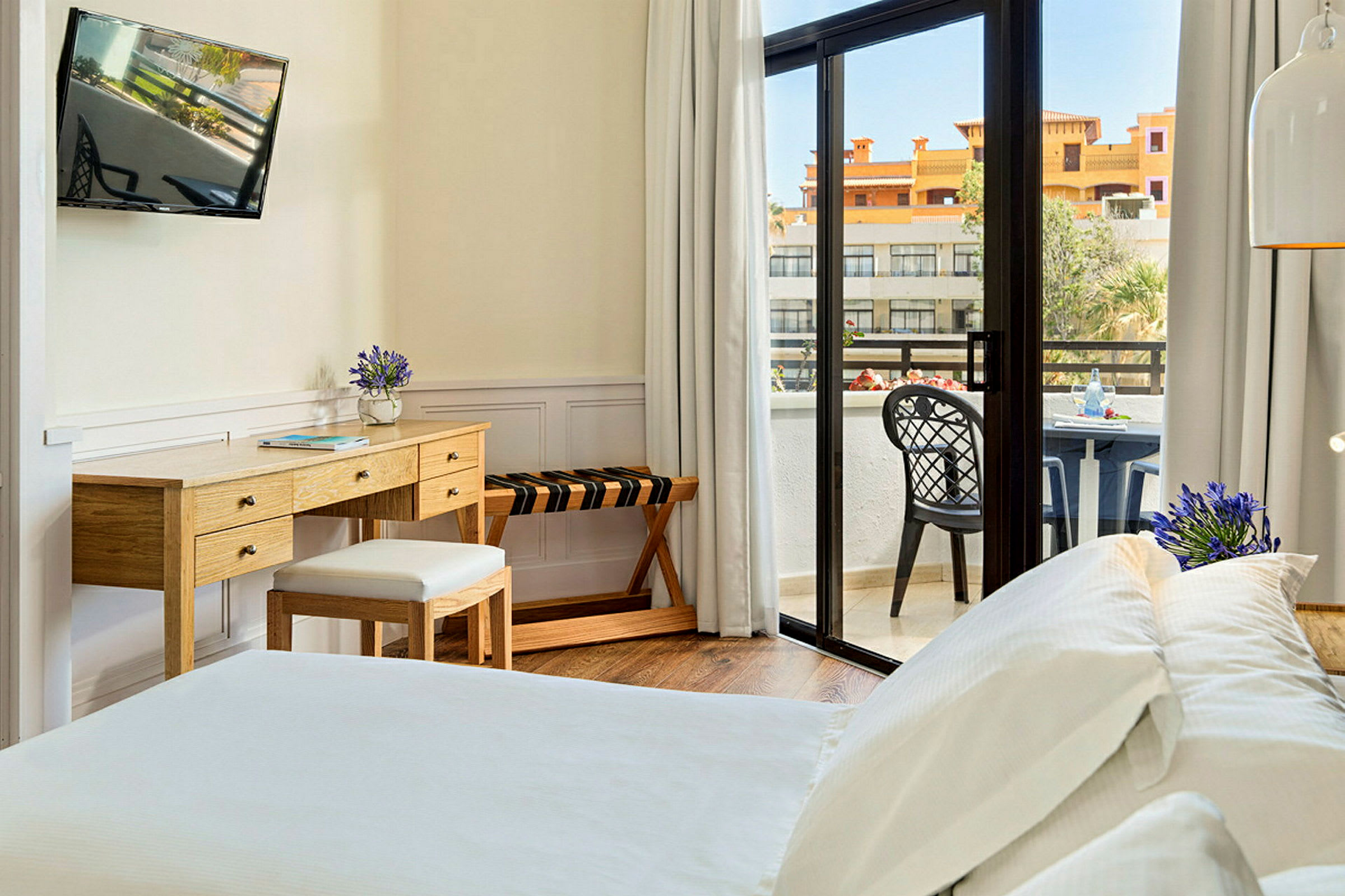 Et hotelværelse med en seng, skrivebord og en balkon med udsigt. (AI-genereret tekst)