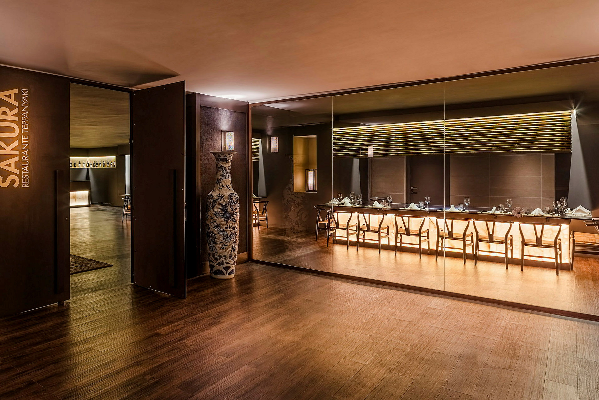 En elegant restaurant med moderne indretning, et stort bord og stole foran en oplyst væg. (AI-genereret tekst)