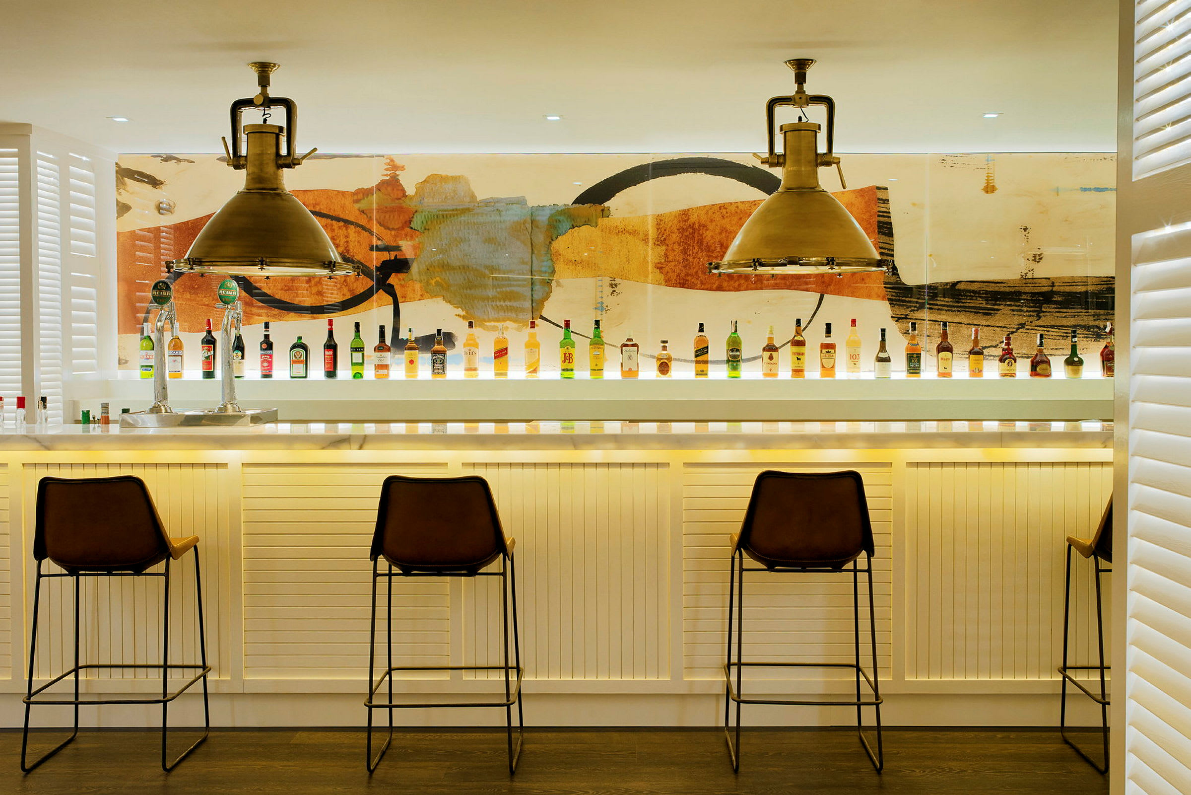 Billede af en moderne bar med stole og flasker opstillet på bardisken foran en farverig baggrund. (AI-genereret tekst)