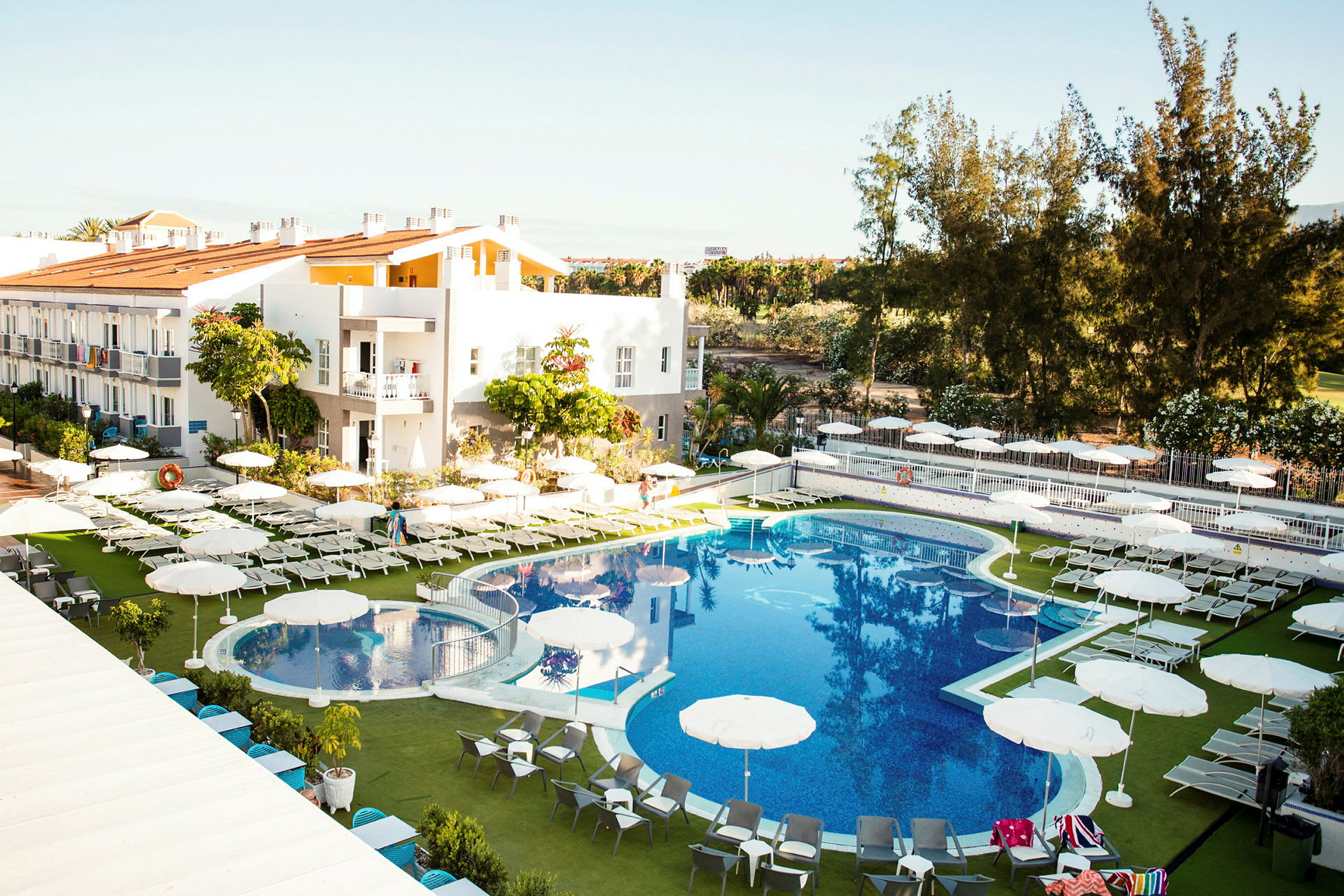 Hotelområde med pool, liggestole og parasoller. (AI-genereret tekst)