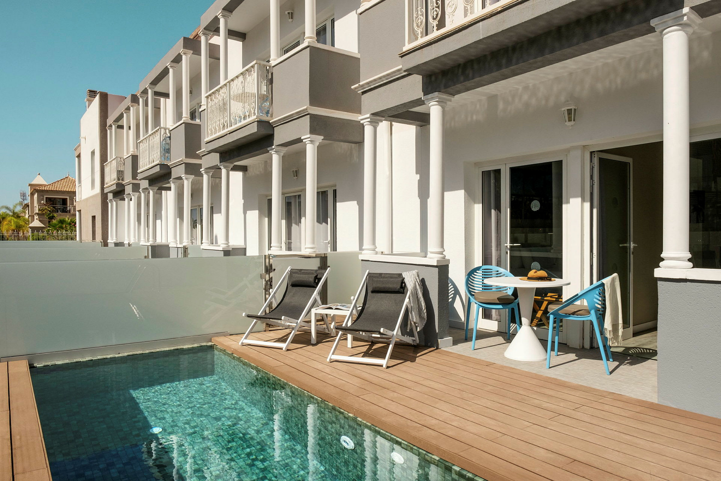 Bygninger med terrasse ved siden af en lille pool. (AI-genereret tekst)