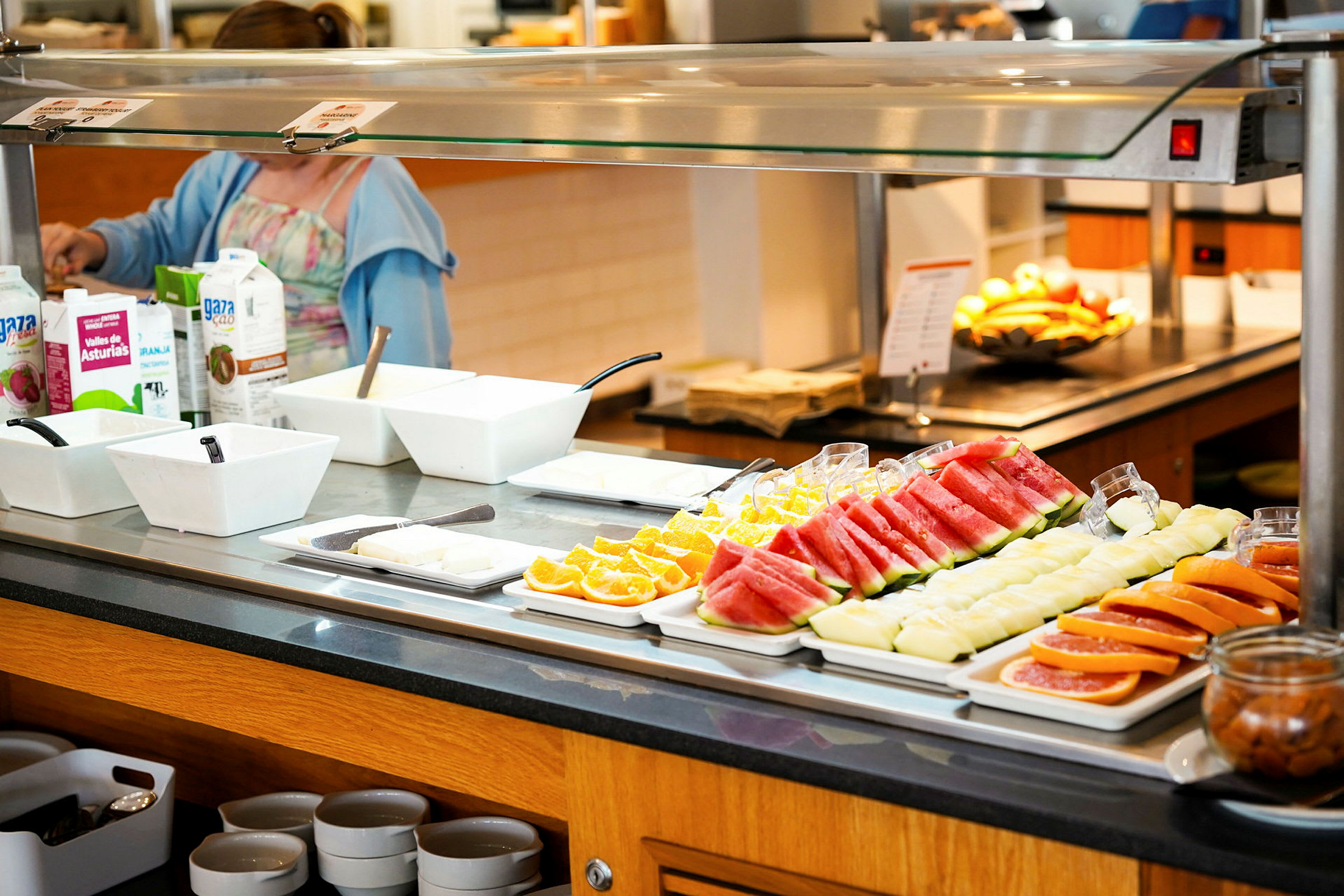 Billede af en buffet med udskåret frugt og drikkevarer. En person kan ses ved buffeten. (AI-genereret tekst)