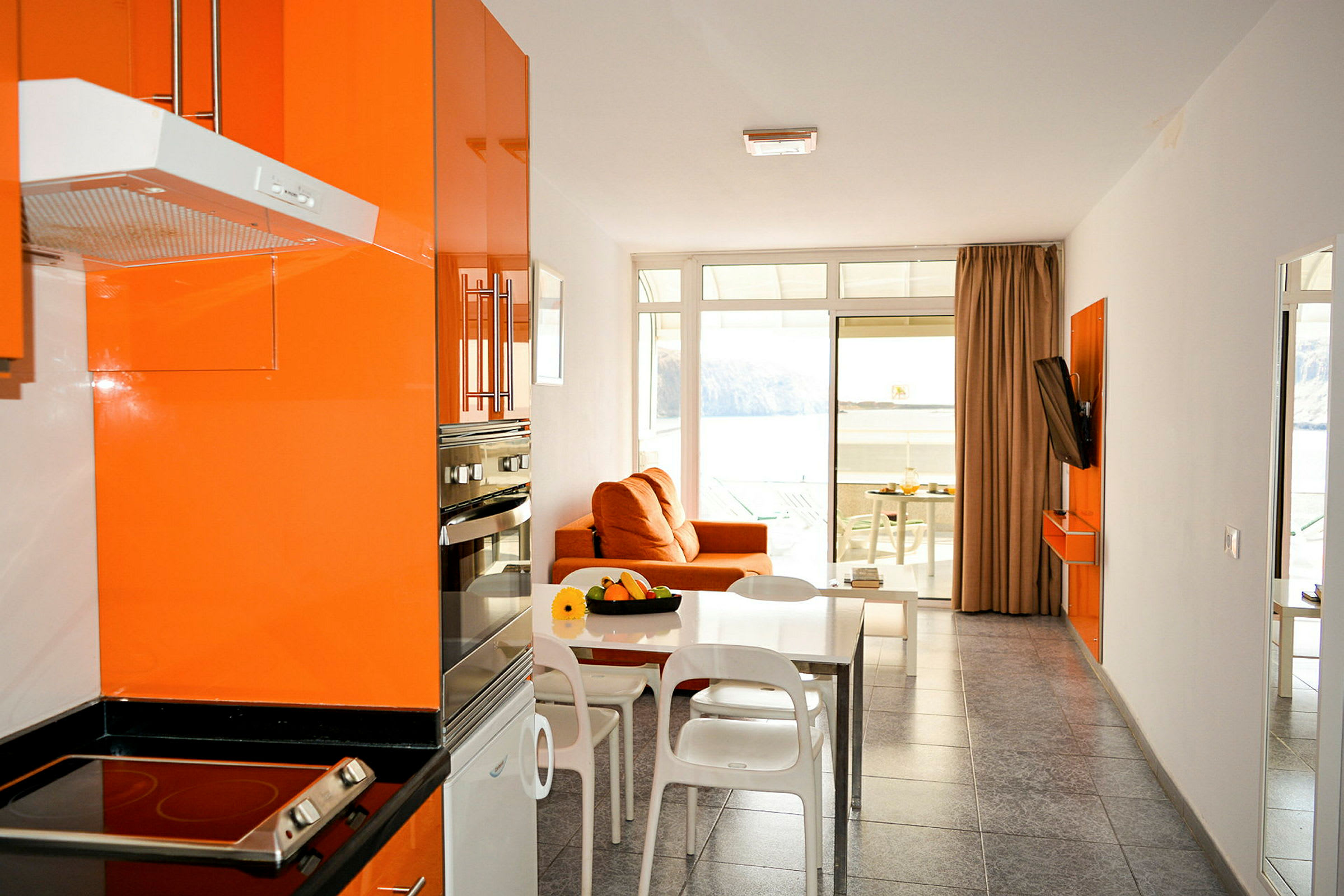Moderne køkken og stue med orange indretning og udsigt til havet. (AI-genereret tekst)
