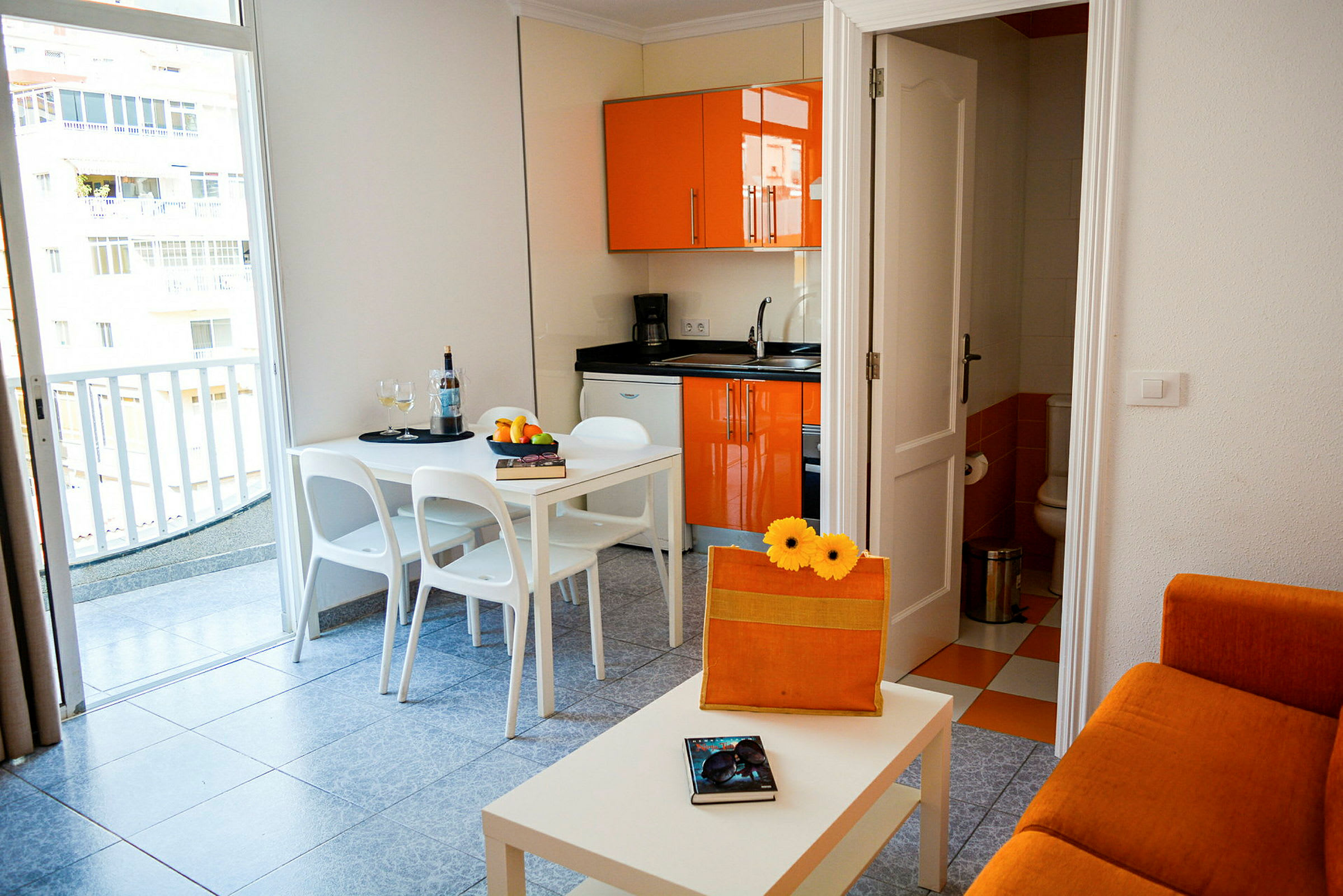 En lille lejlighed med orange køkkenindretning, en hvid spiseplads og en sofa. (AI-genereret tekst)