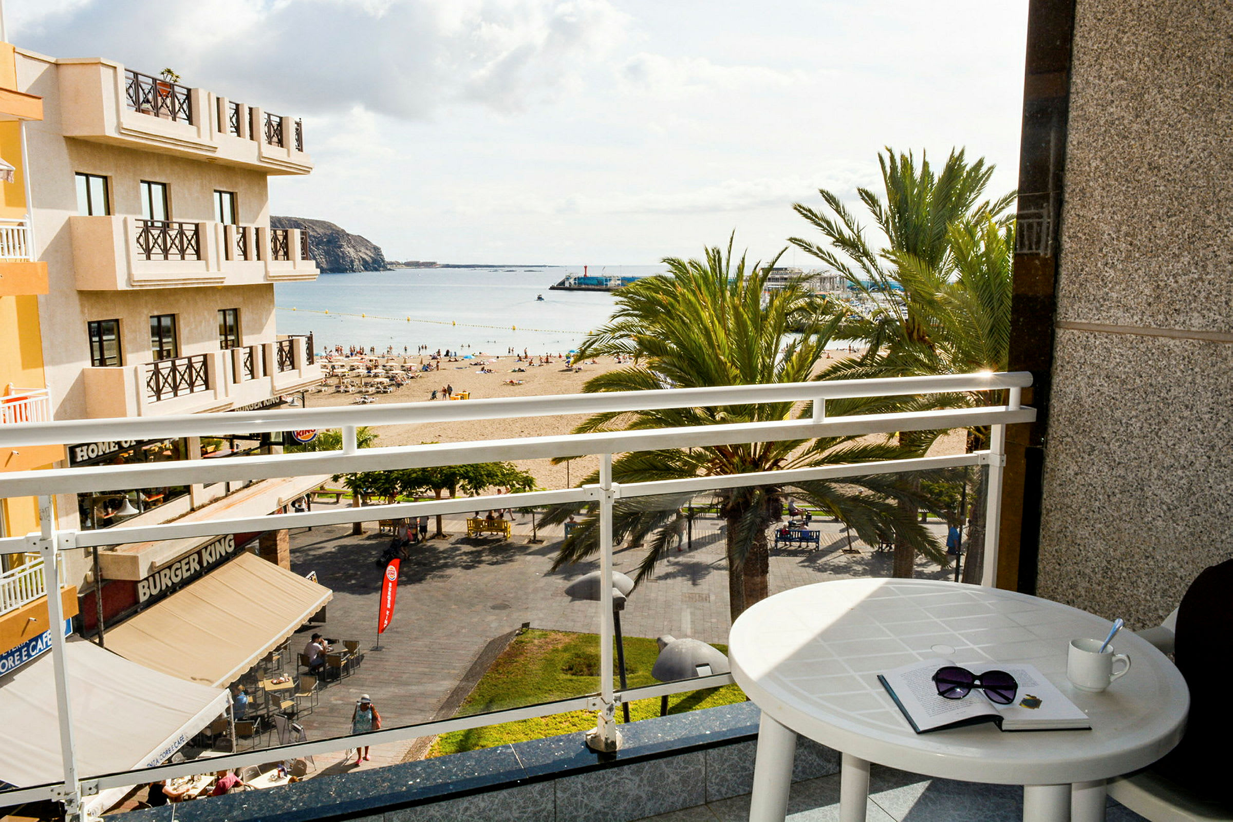 Udsigt fra et hotelværelse med en balkon mod en strand og havet. (AI-genereret tekst)