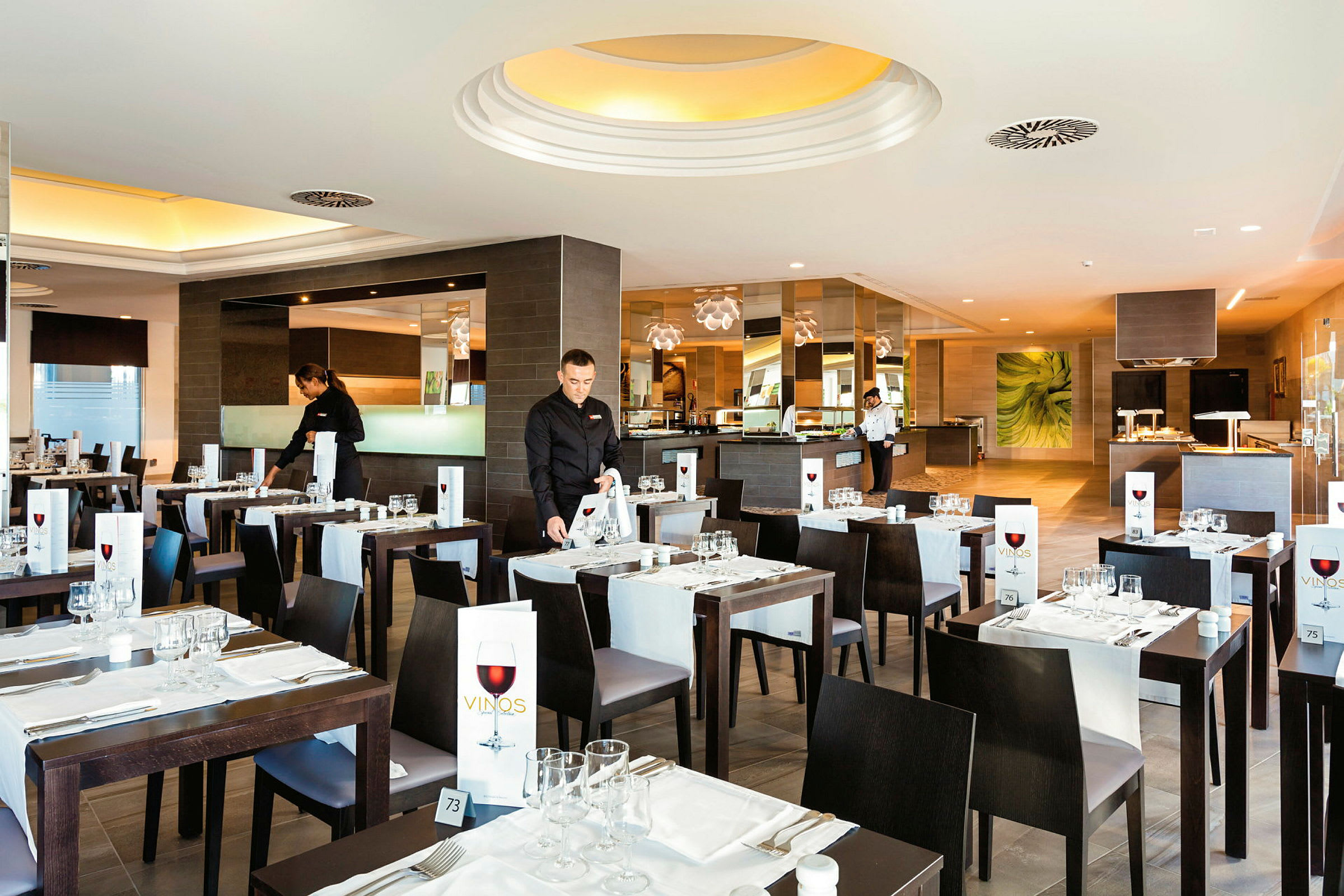 En restaurant med stilfuldt dækkede borde og tjenere, der forbereder sig til gæsterne. (AI-genereret tekst)
