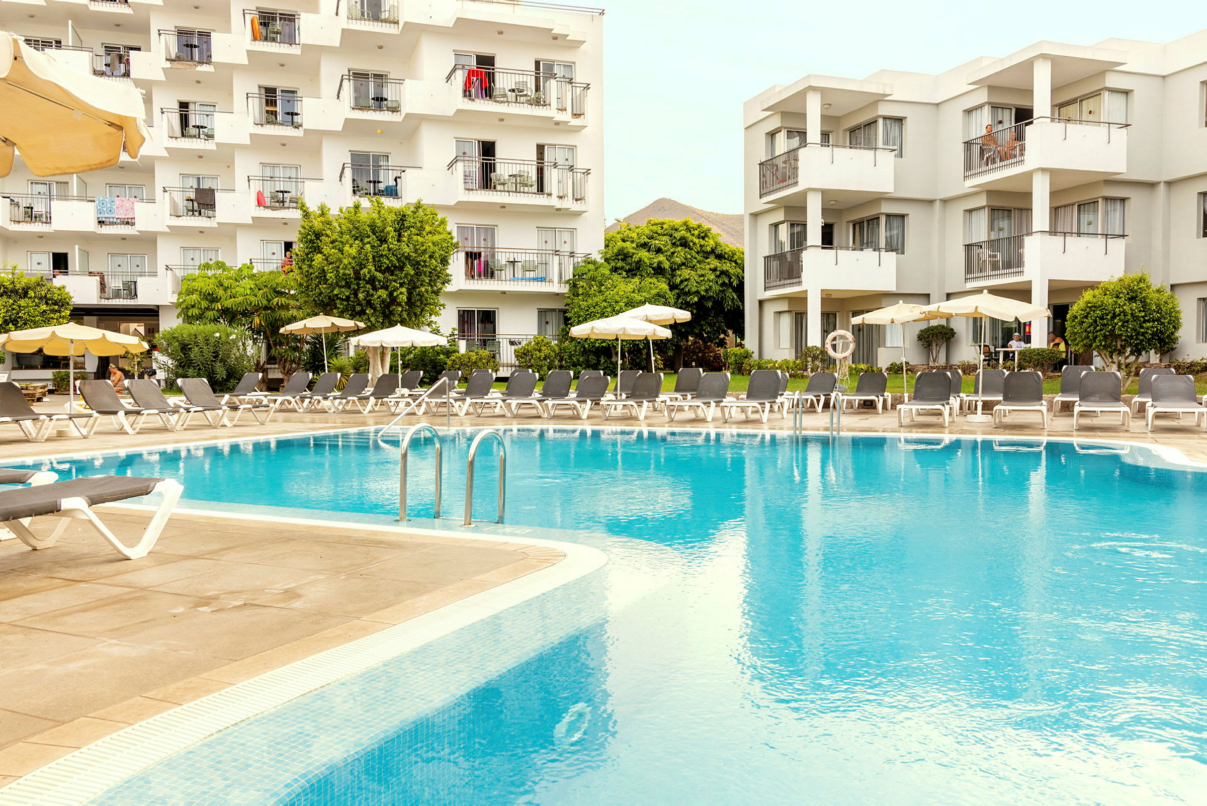 Hotelbygning med altaner ved en stor udendørs pool. (AI-genereret tekst)
