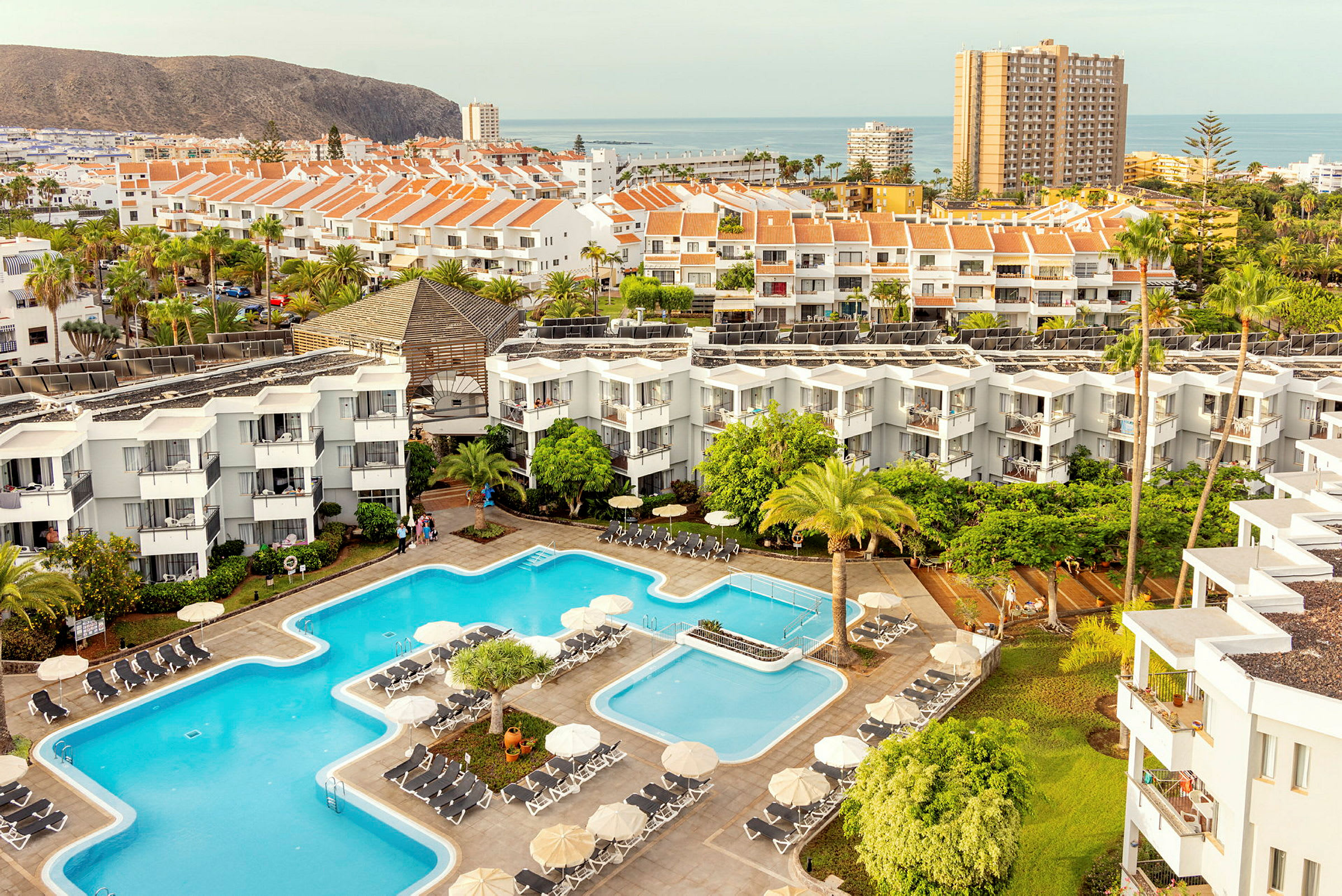 Udsigt over hotelområde med pools, bygninger og omkringliggende landskab. (AI-genereret tekst)