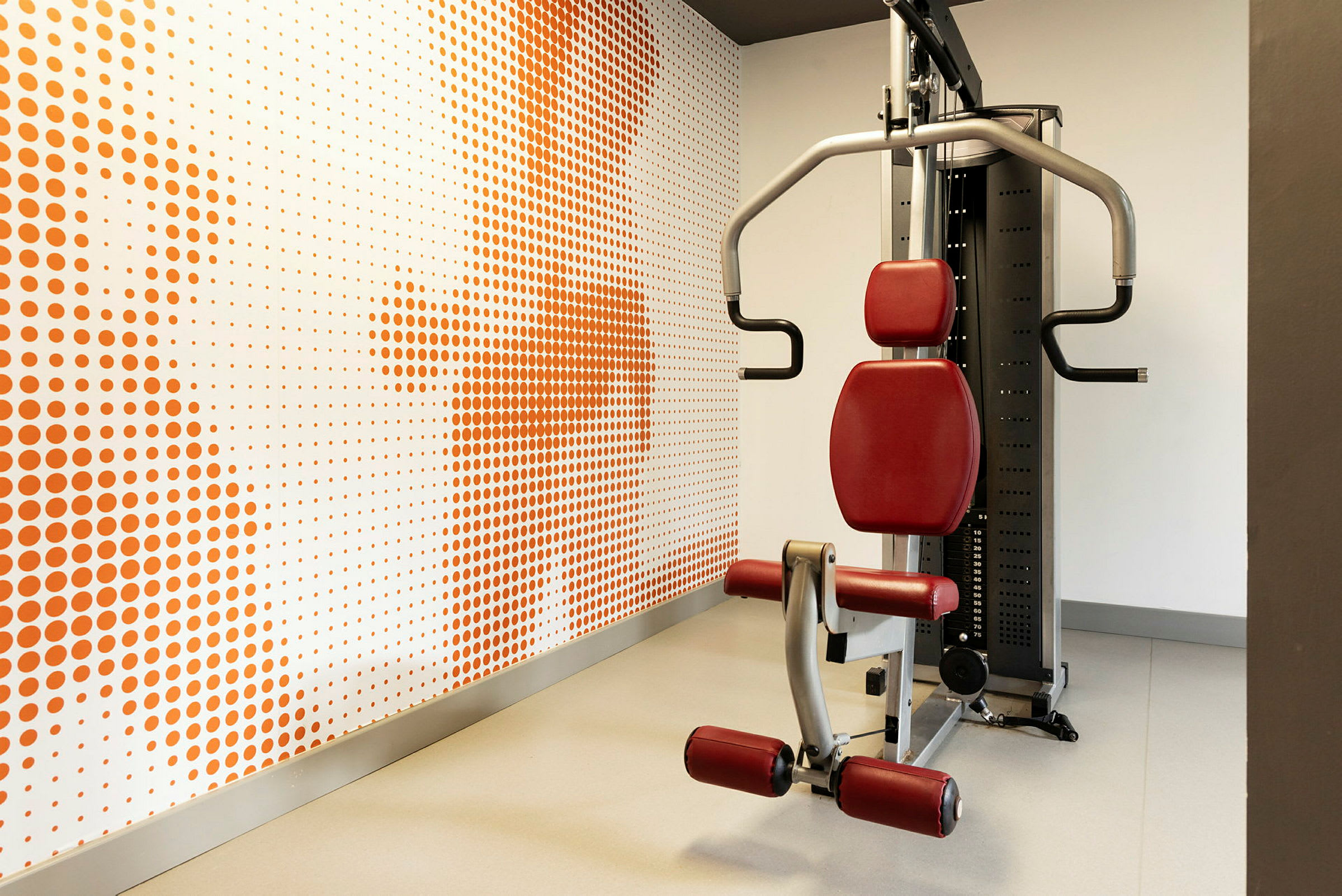 Træningsmaskine i et fitnesscenter, med en baggrund af vægdekoration med orange prikker. (AI-genereret tekst)