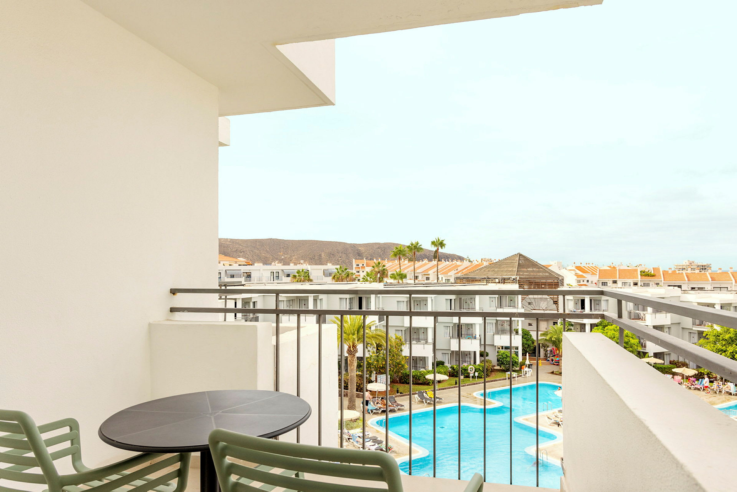 Udsigt fra en balkon over hotelområdet med pool og omkringliggende bygninger. (AI-genereret tekst)