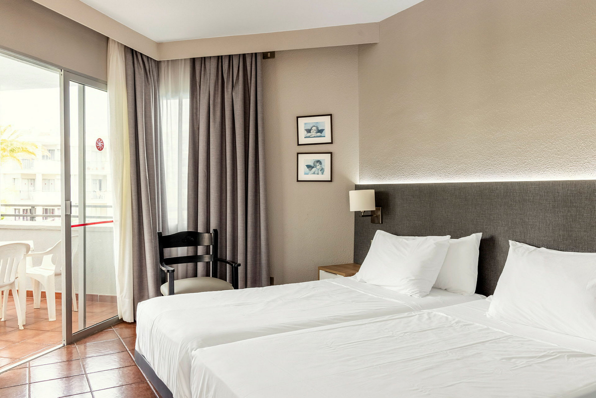 Hotelværelse med to enkeltsenge, en stol og en altan. (AI-genereret tekst)