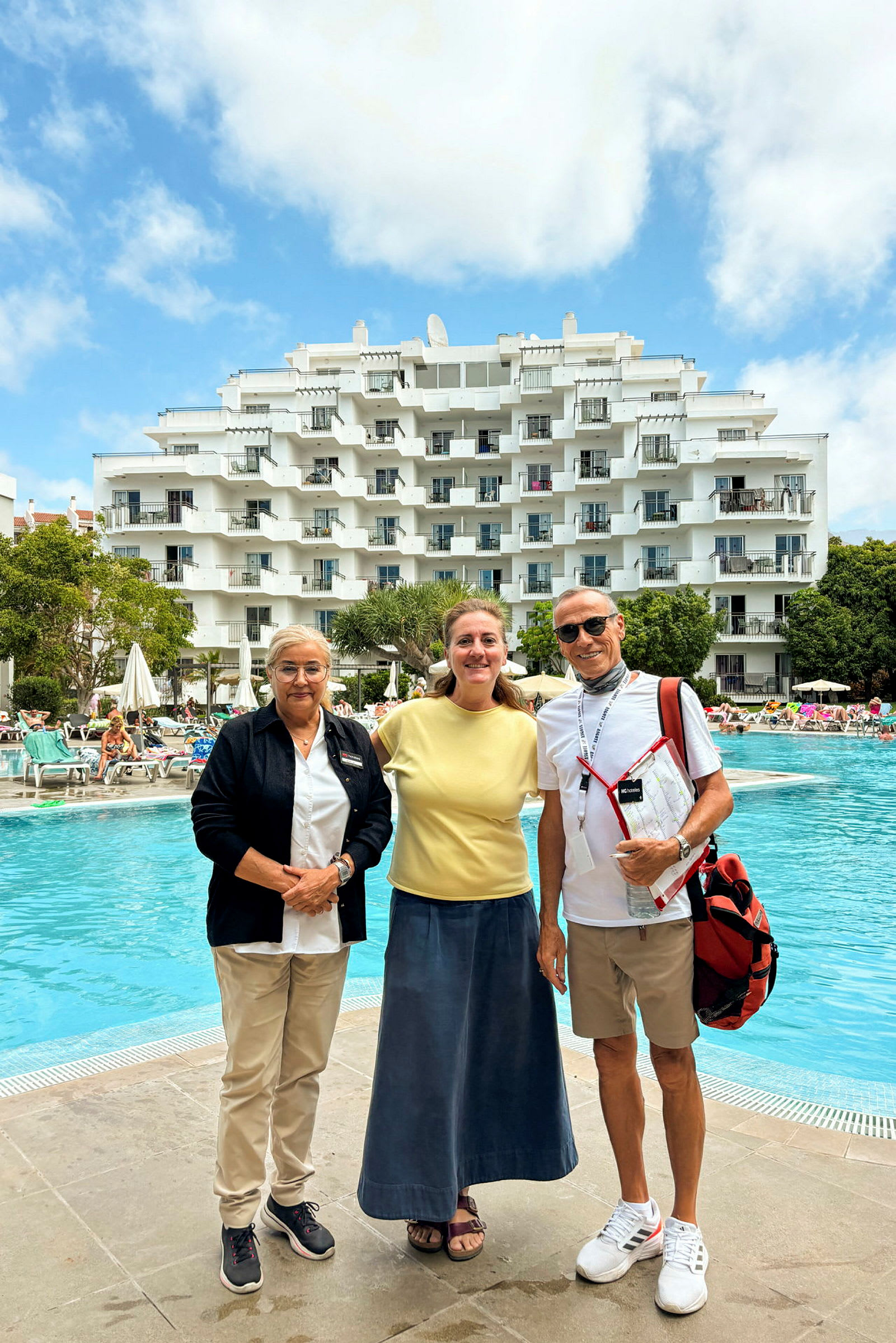 Hotelbygning ved en udendørs swimmingpool med mennesker og liggestole. (AI-genereret tekst)