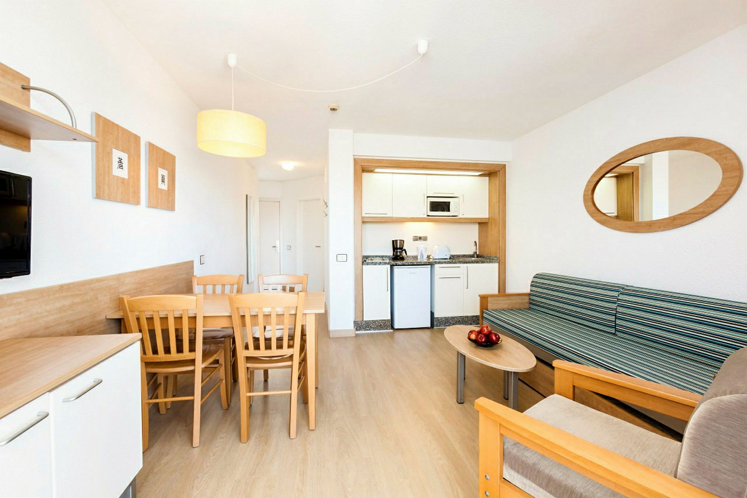 Et moderne hotelværelse med en lille køkkenkrog, en spiseplads med bord og stole samt en siddegruppe med sofa og sofabord. (AI-genereret tekst)