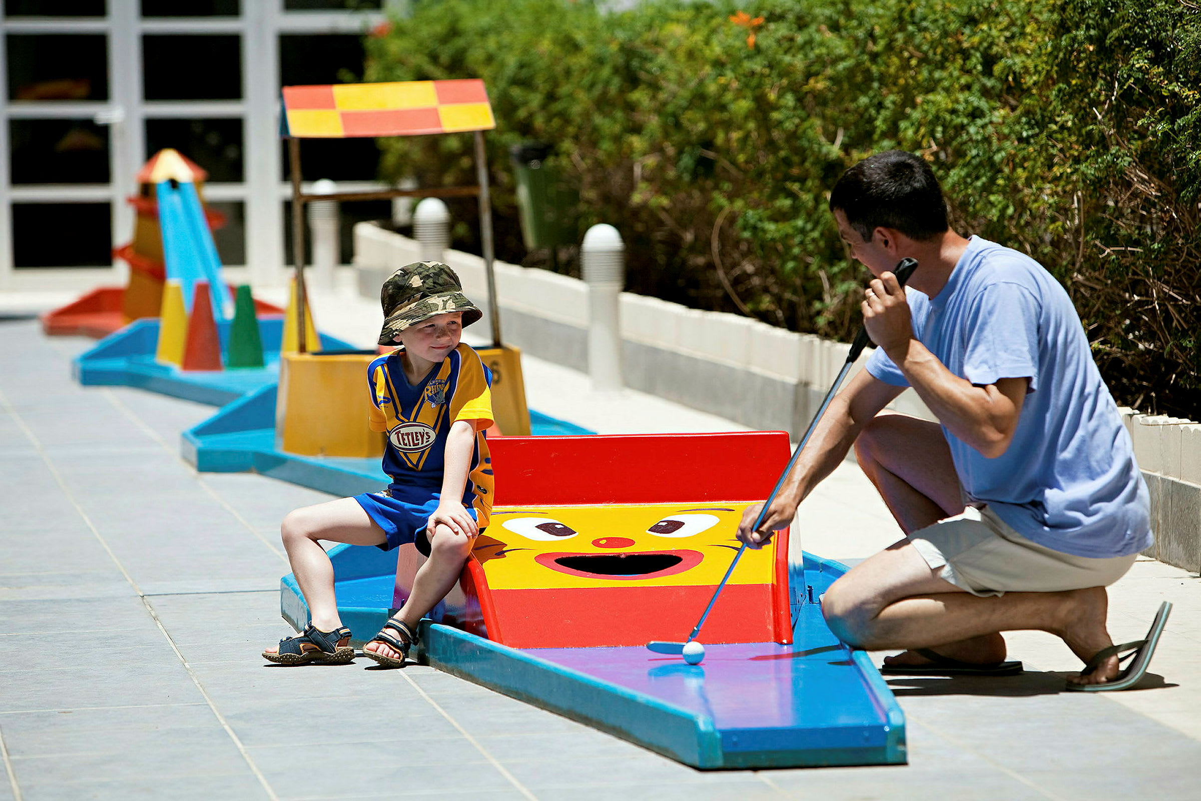 Personer spiller minigolf udendørs på en bane med farverige forhindringer. (AI-genereret tekst)