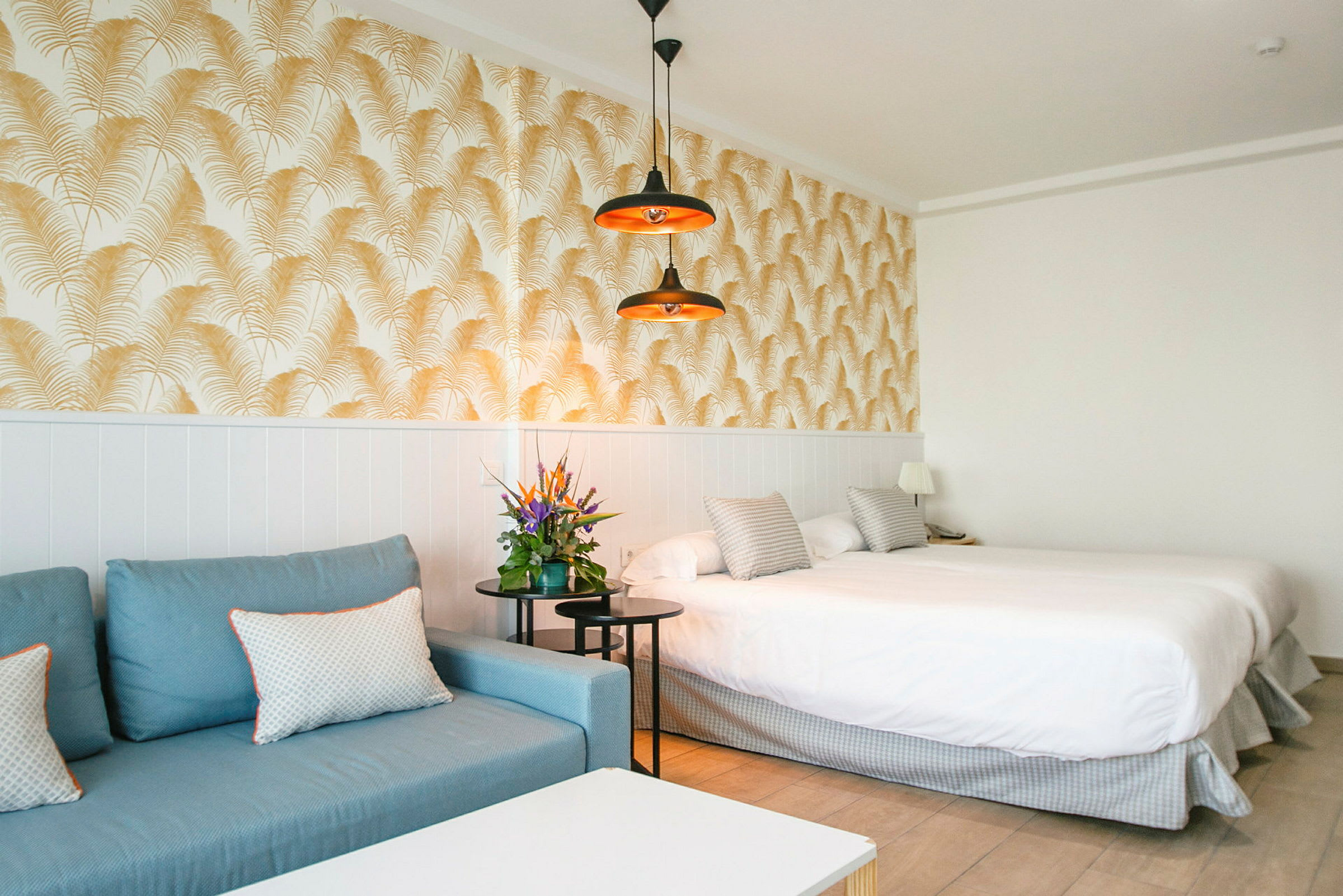 Hotelværelse med blå sofa, dobbeltseng og dekorativ tapet. (AI-genereret tekst)