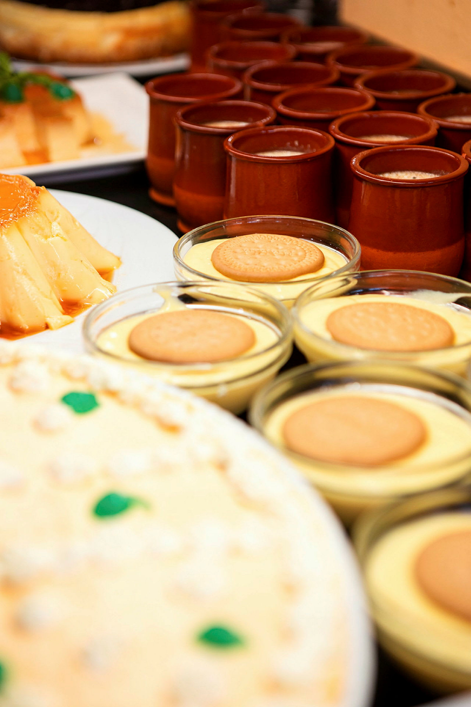 En række små skåle med dessert toppet med kiks, bagved ses flere desserter og små krukker. (AI-genereret tekst)