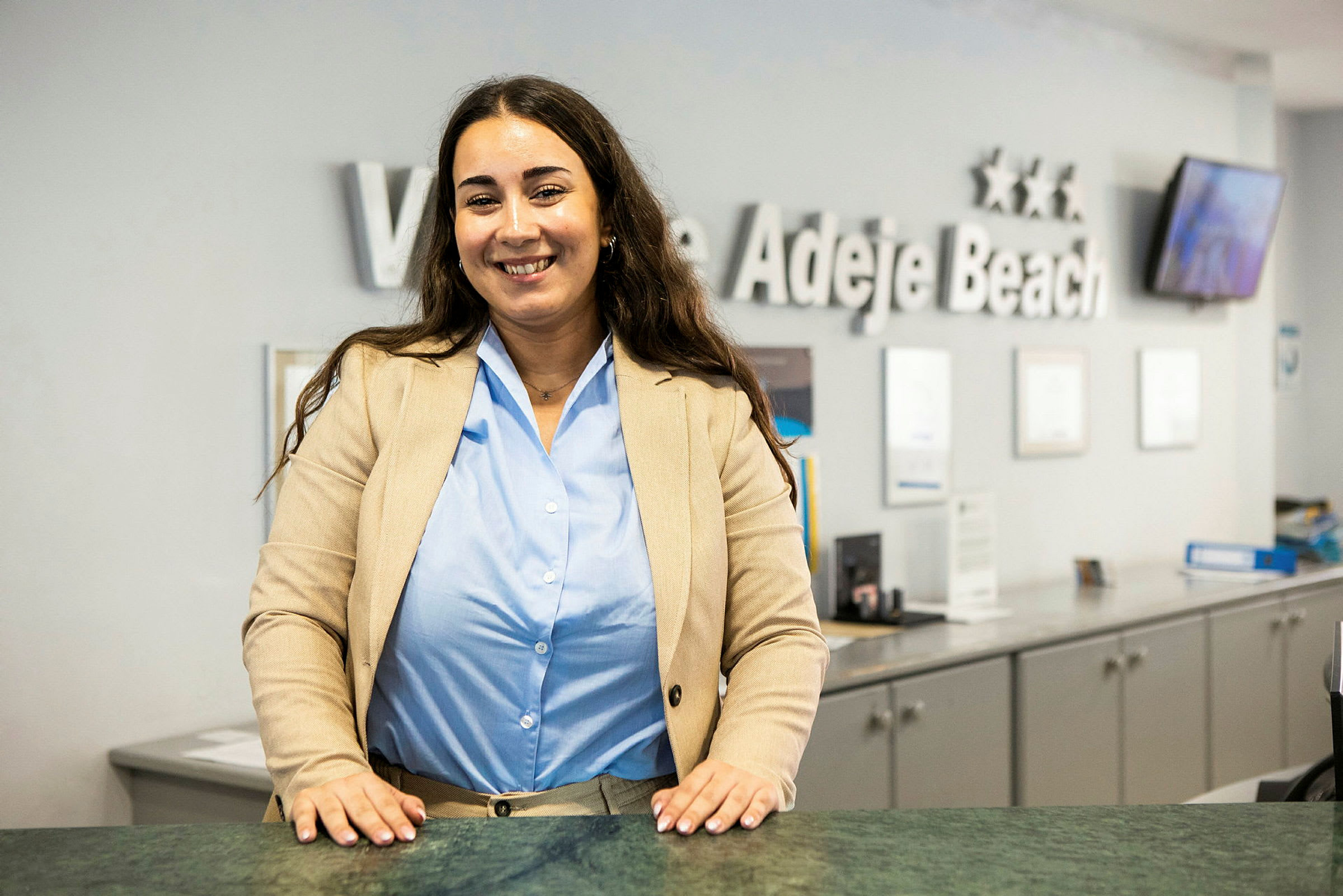 Receptionist står ved en receptionsskranke med et skilt i baggrunden. (AI-genereret tekst)