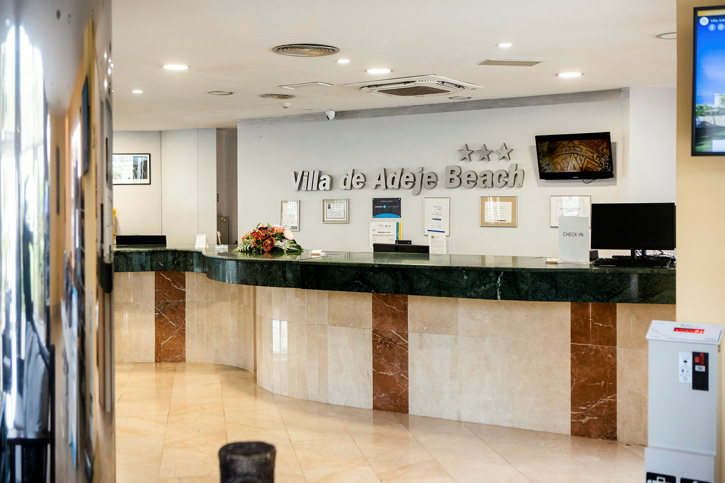 Hotelreception med marmordisk og skilt, der viser "Villa de Adeje Beach". (AI-genereret tekst)