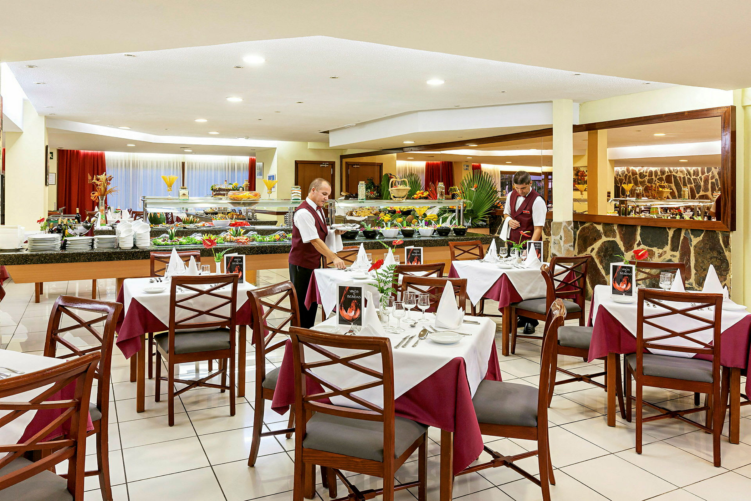 En restaurant med dækkede borde, veludstyrede buffeter og en tjener i uniform. (AI-genereret tekst)