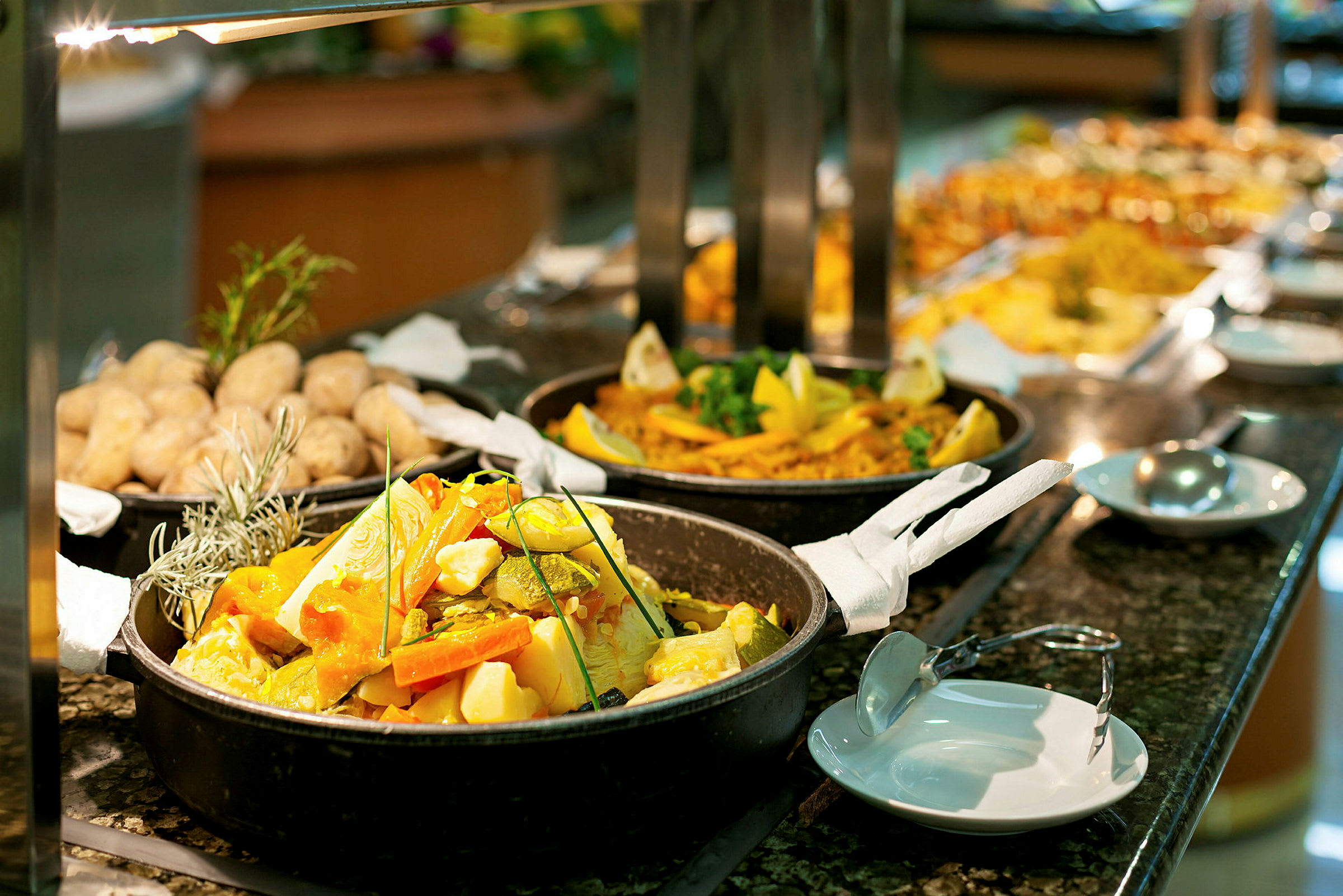 Buffet med forskellige retter, herunder grøntsager i en gryde og bagte kartofler. (AI-genereret tekst)