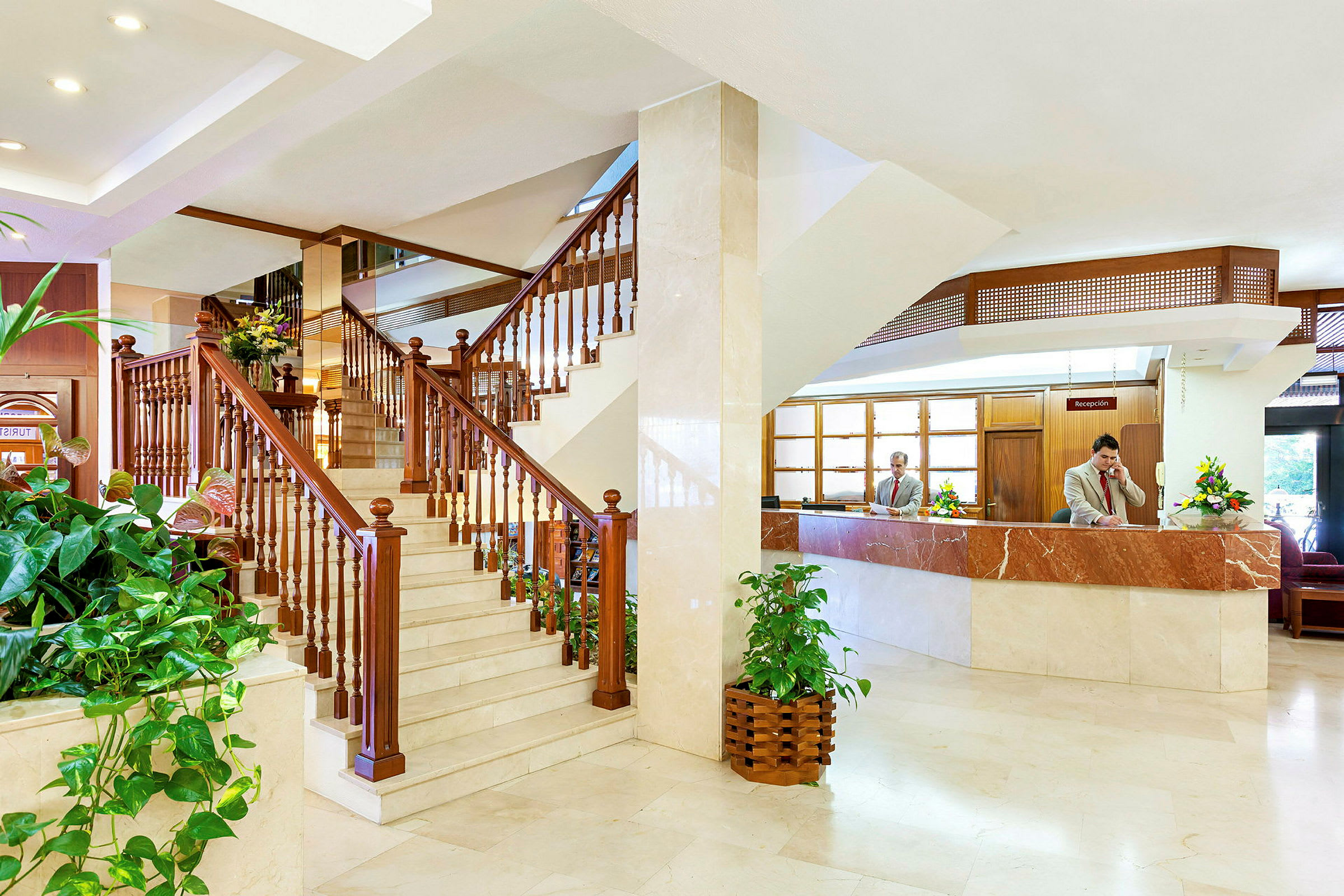 Hotellets lobby med en trætrappe og receptionen. (AI-genereret tekst)