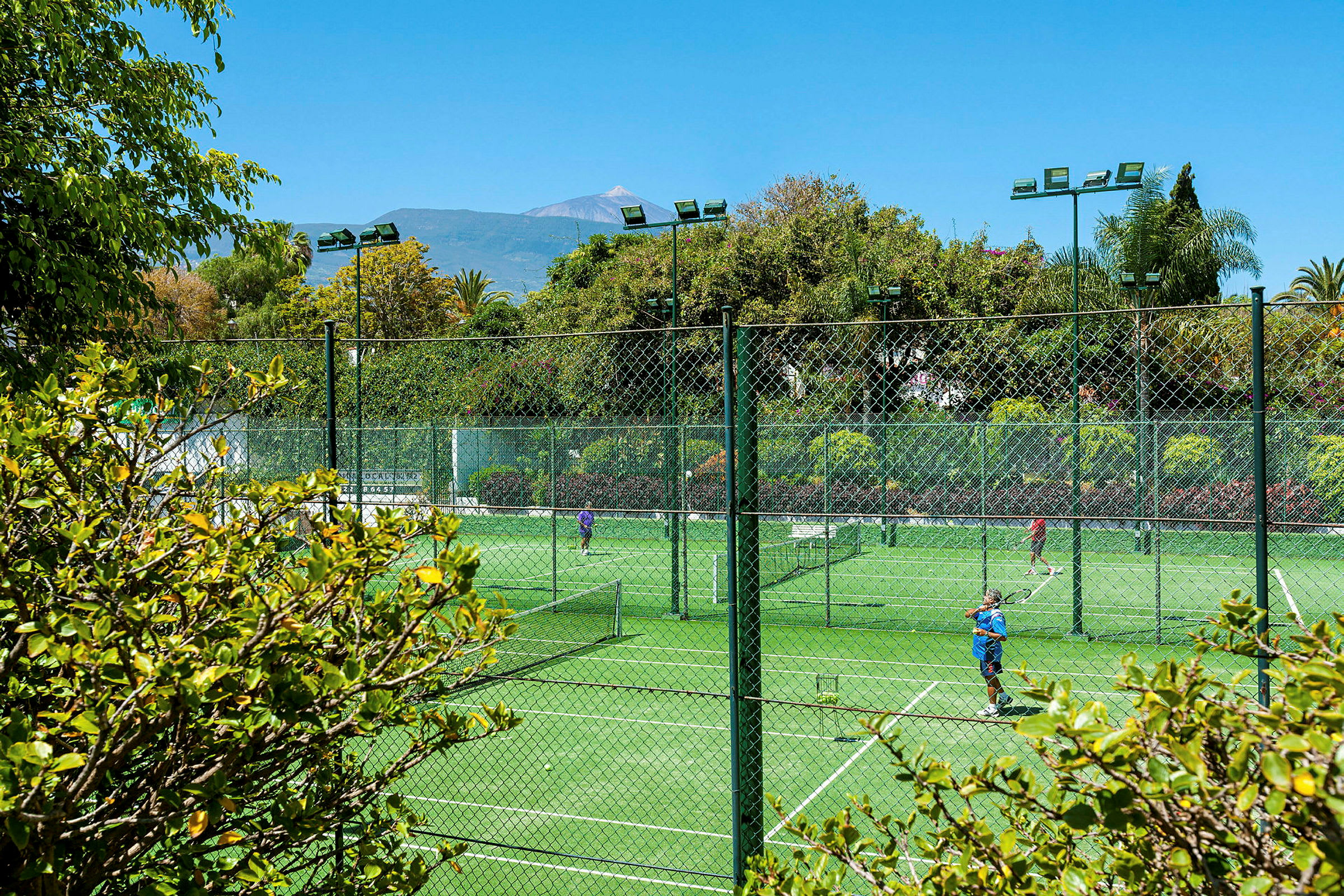 Udendørs tennisbaner omgivet af grønne områder og træer. (AI-genereret tekst)