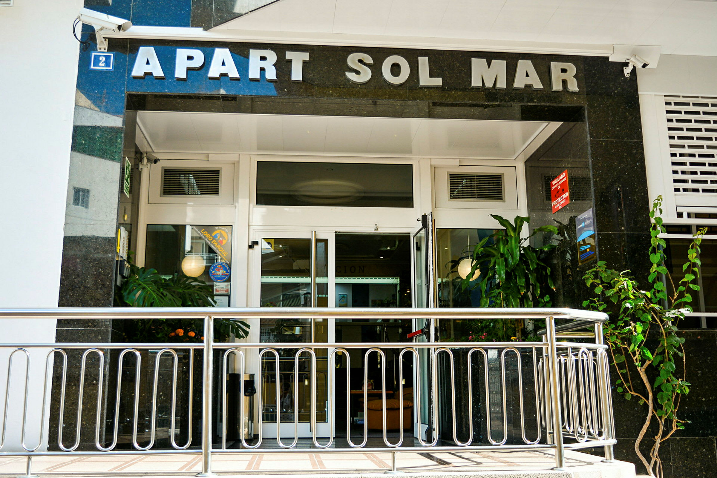 Indgang til Apart Sol Mar med glasdøre og planter. (AI-genereret tekst)