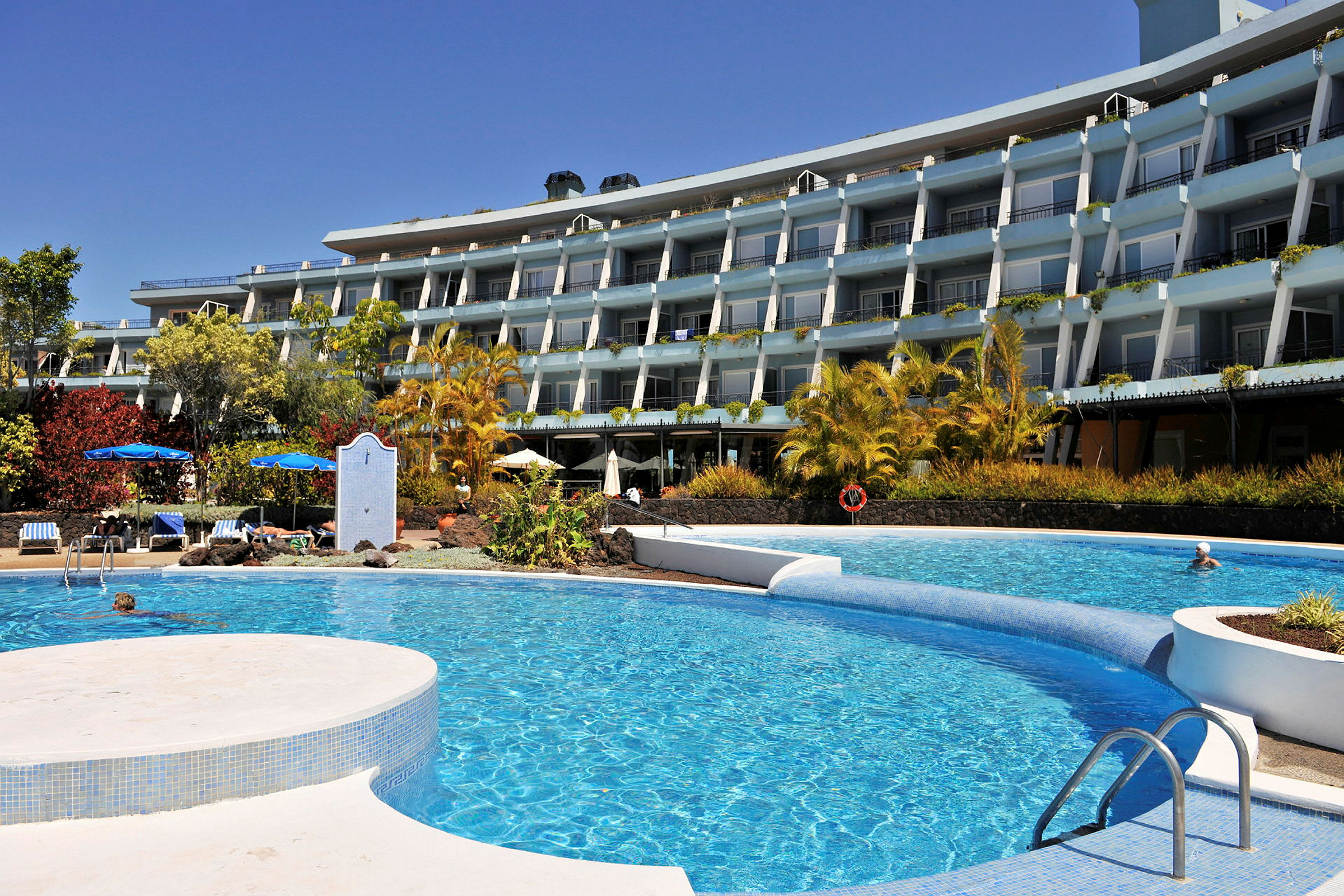 Et hotel med flere etager ses bag en pool i forgrunden. (AI-genereret tekst)