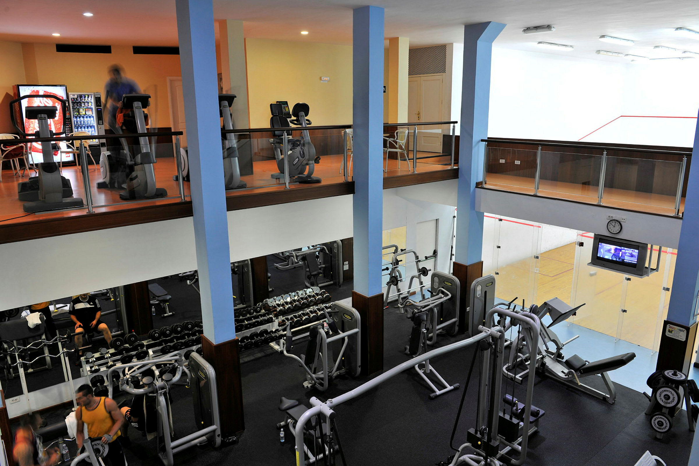 To-etagers fitnesscenter med træningsudstyr og en squashbane. (AI-genereret tekst)